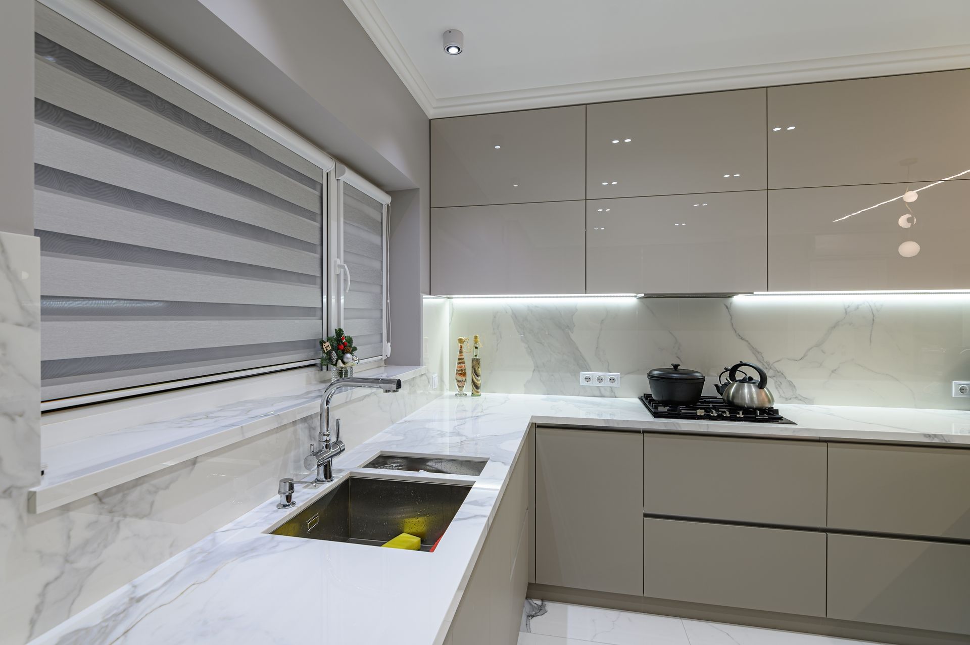 Modern white kitchen with sink, window blinds, and glossy cabinets under under-cabinet lighting