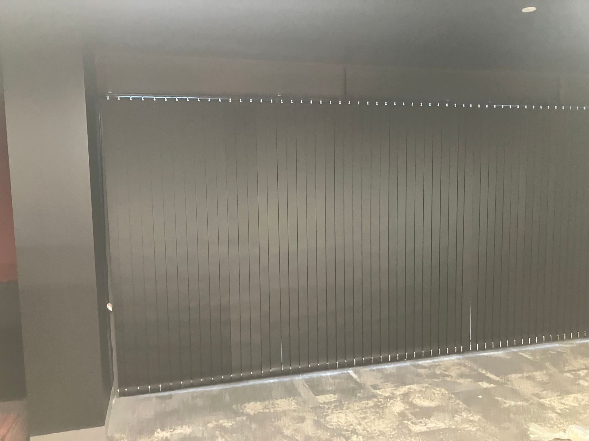 Large black vertical blinds or partition in a hallway with gray walls and floor tiles.