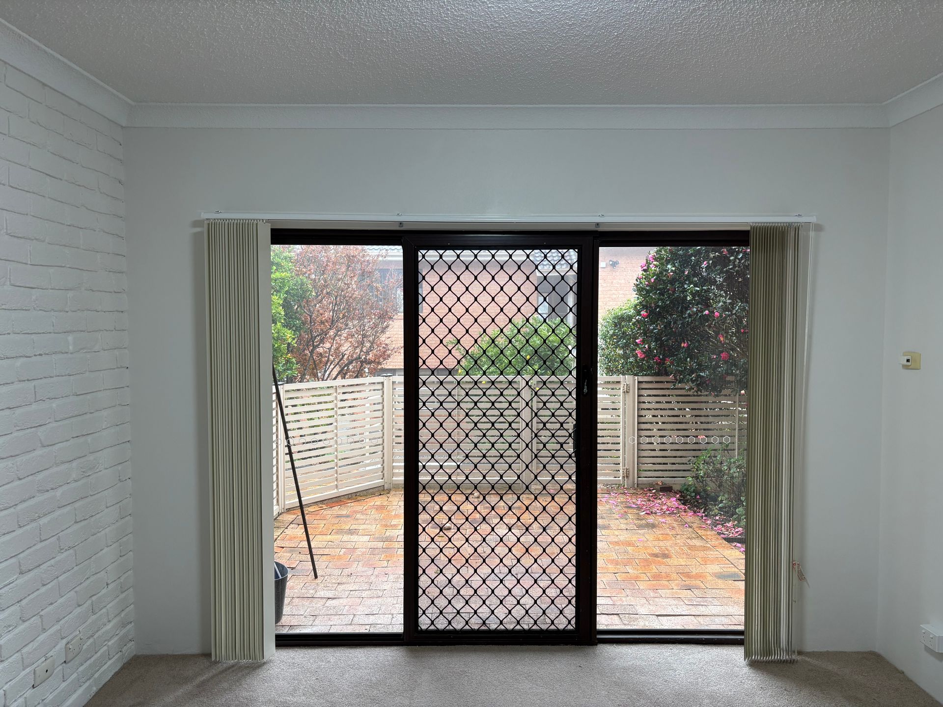 Empty white room with sliding glass doors, curtains, and a fenced backyard patio view.