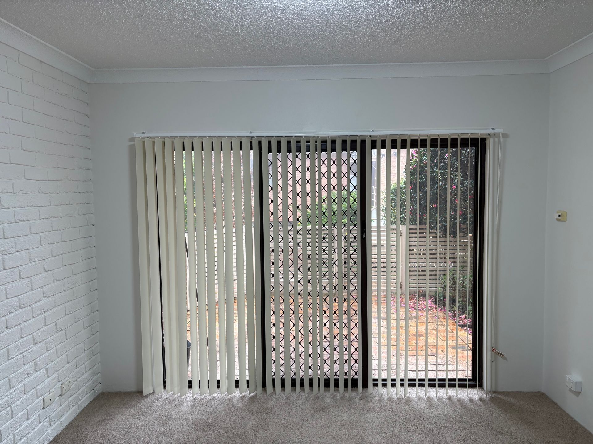 Empty room with white walls, carpet, and sliding glass doors with vertical blinds.