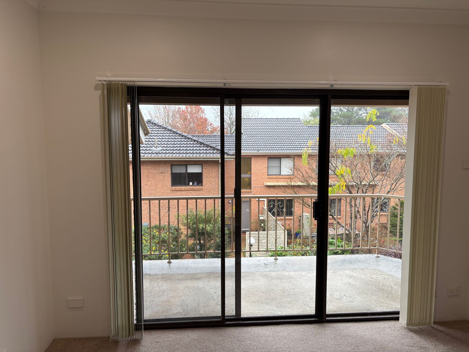 Empty living room with large sliding glass doors opening to a balcony and brick buildings outside