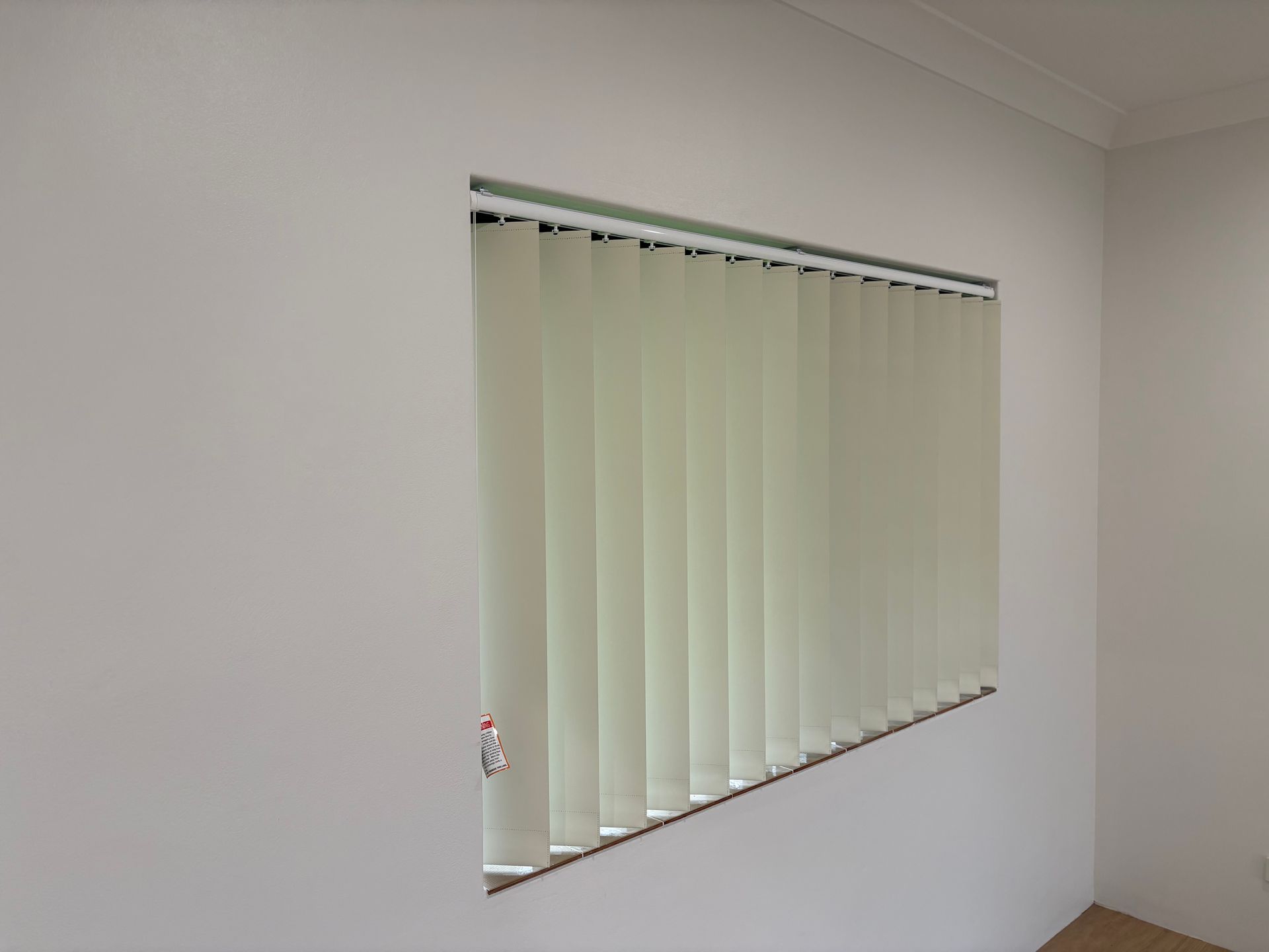 White vertical blinds covering a window in a plain room