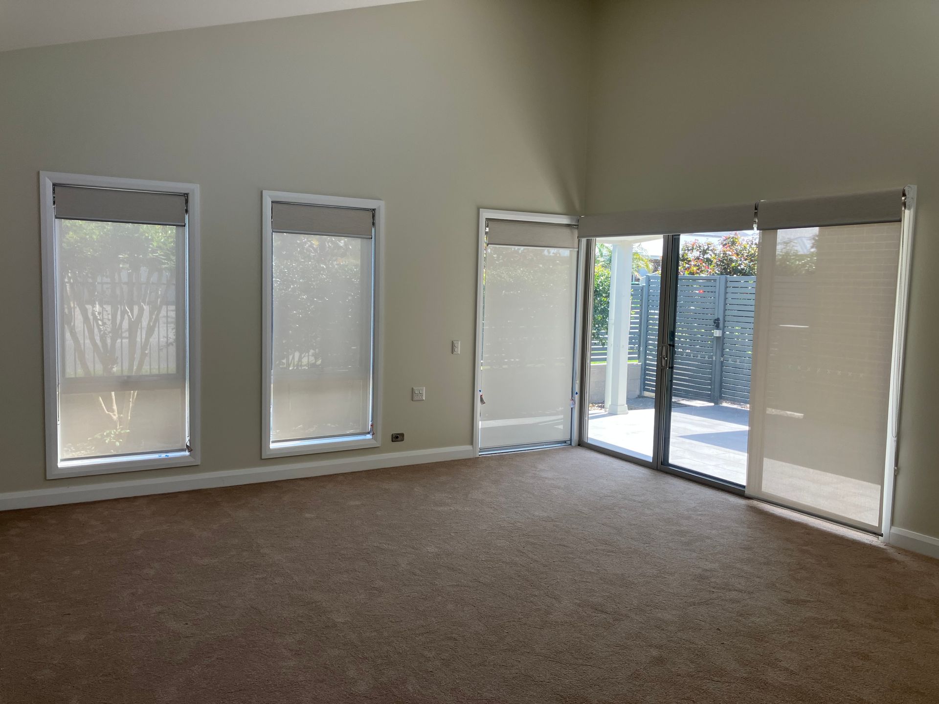 Empty carpeted living room with three windows and a sliding glass door opening to a fenced patio