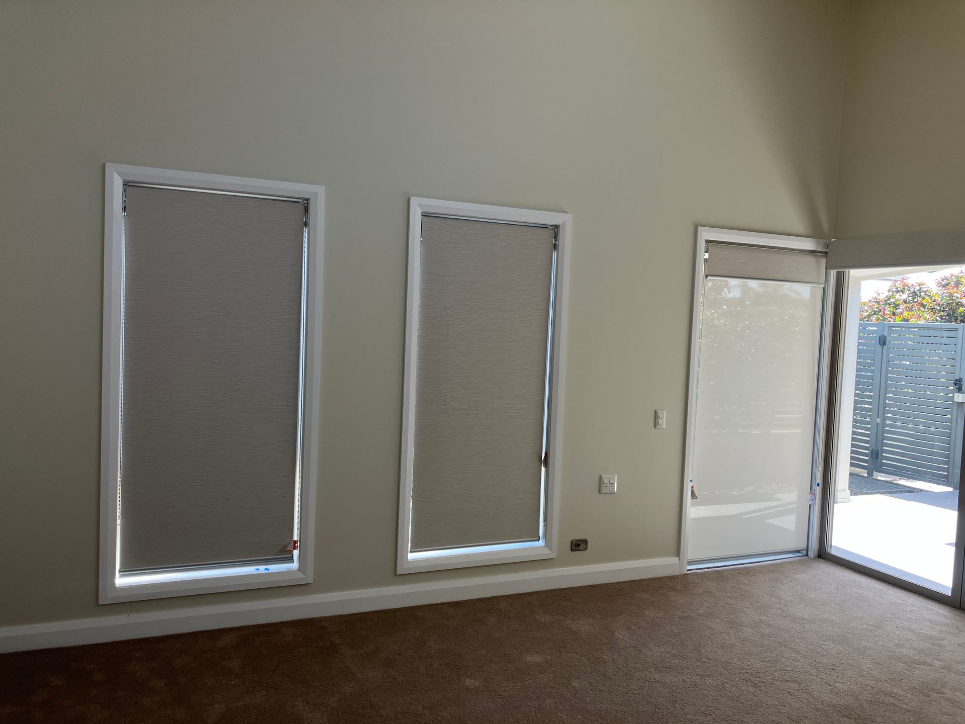 Empty room with tan walls, three windows, and a glass door opening to a patio.