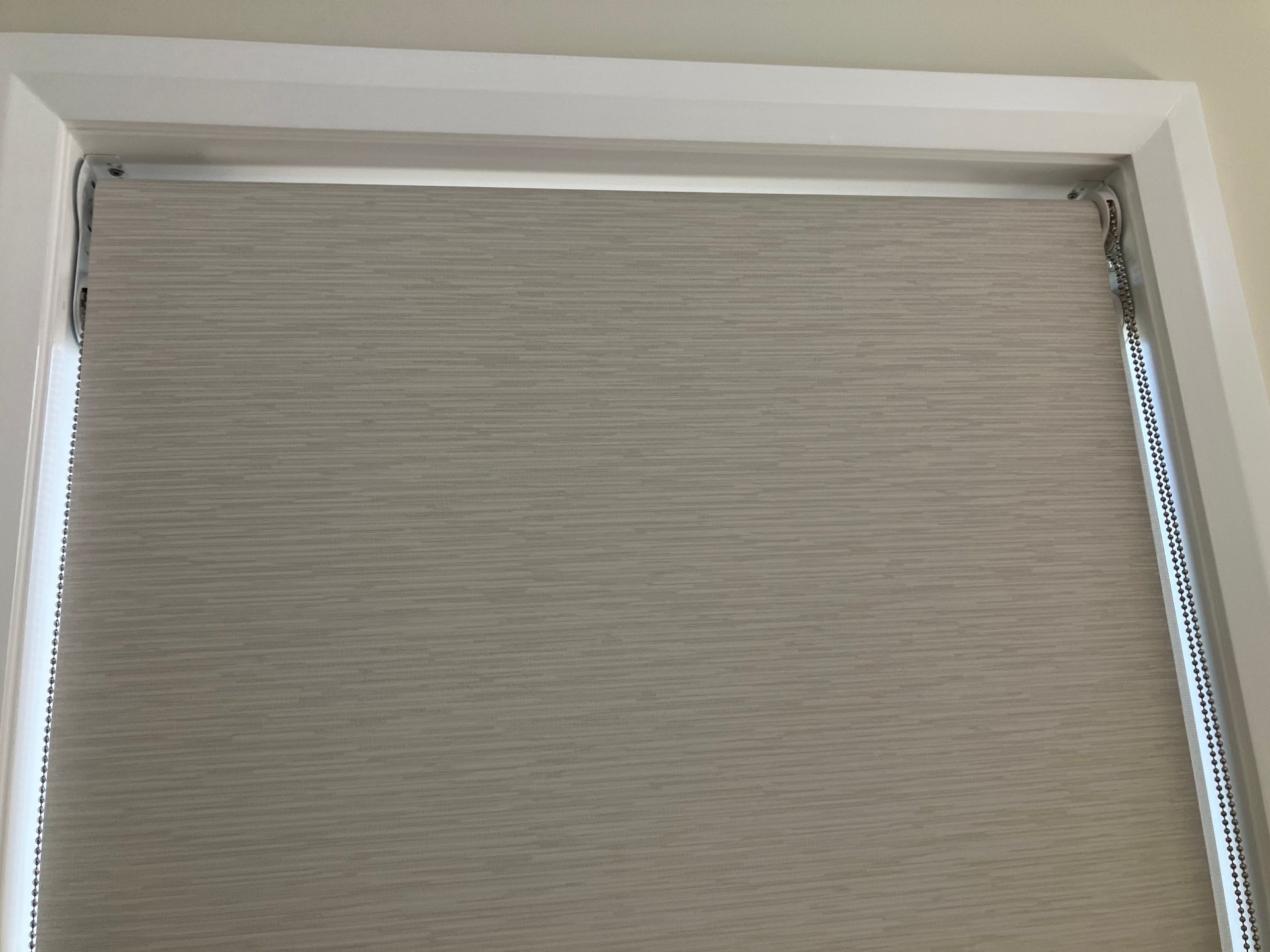 Closed beige window blind inside a white window frame