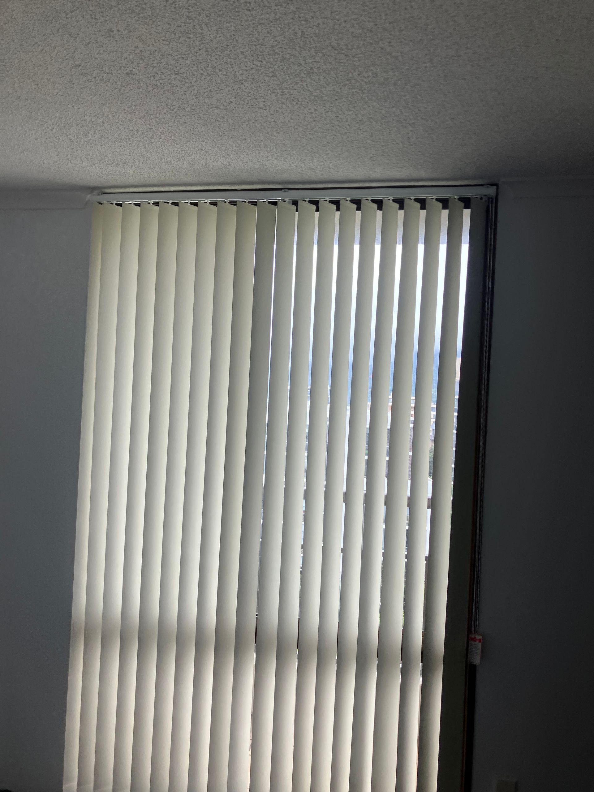 Closed white vertical blinds covering a window in a dim room
