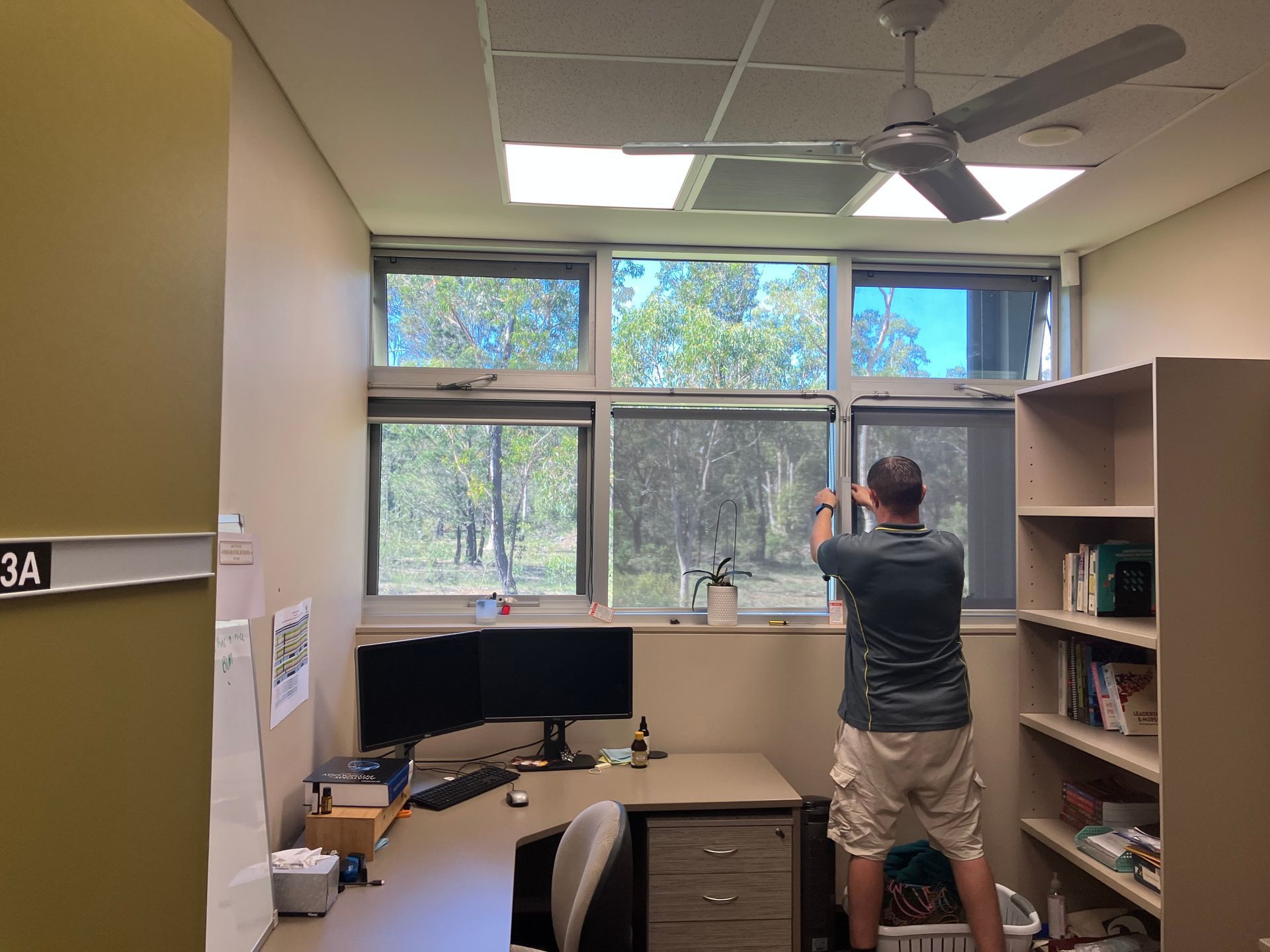 Person taking a photo in an office with desk, shelves, and large windows.