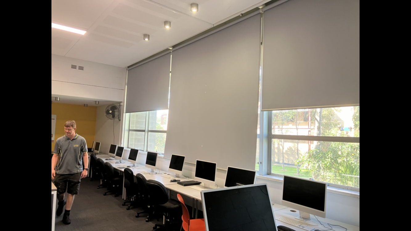Office classroom with rows of computers, large windows, and a person walking near the front