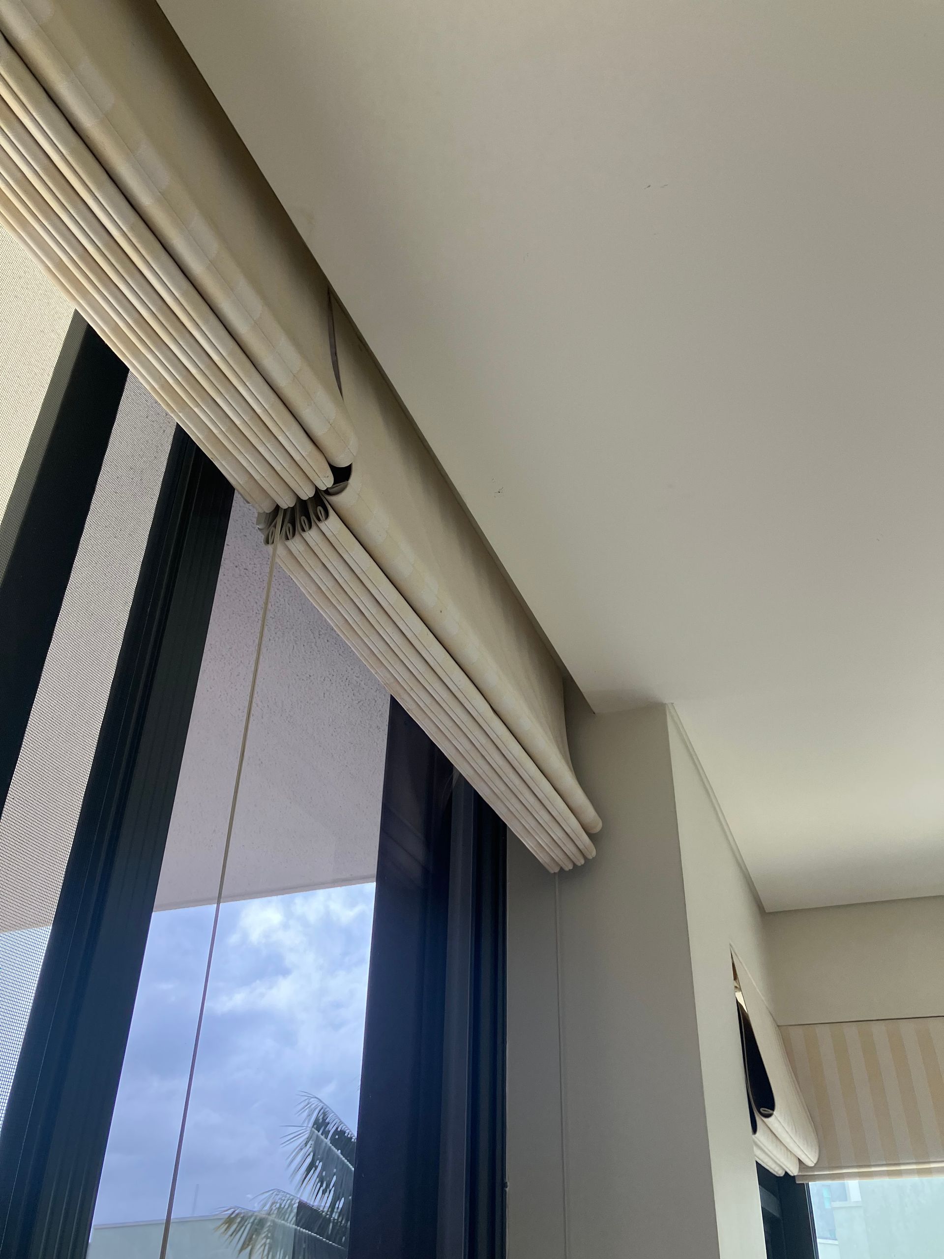 Window with white blinds partially open beside a ceiling and blue-tinted glass door.