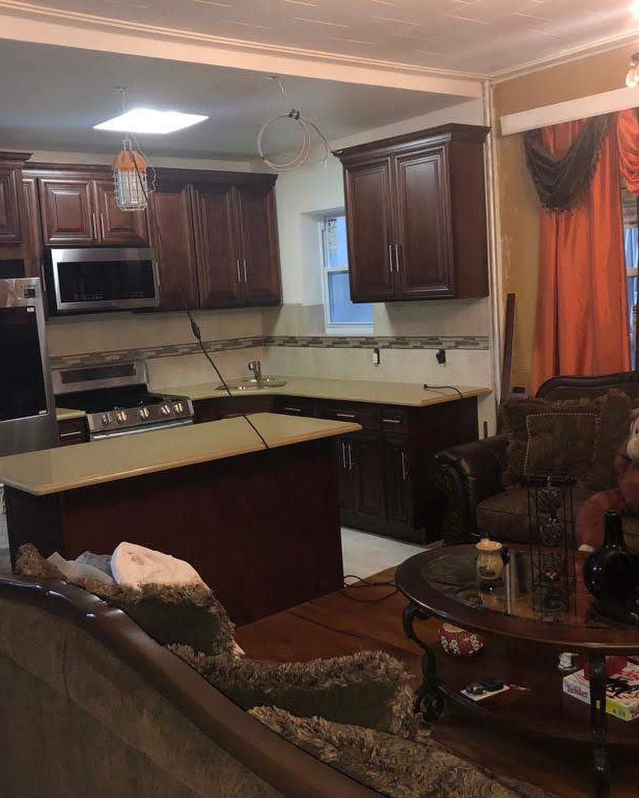 Kitchen with brown cabinets, island, and appliances, next to living room with couch and chair.