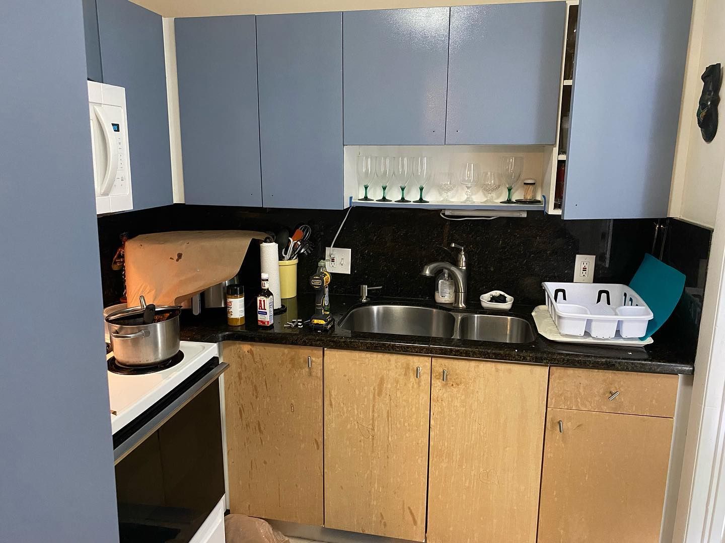 Small kitchen with blue upper cabinets, exposed lower cabinets, and a double sink.