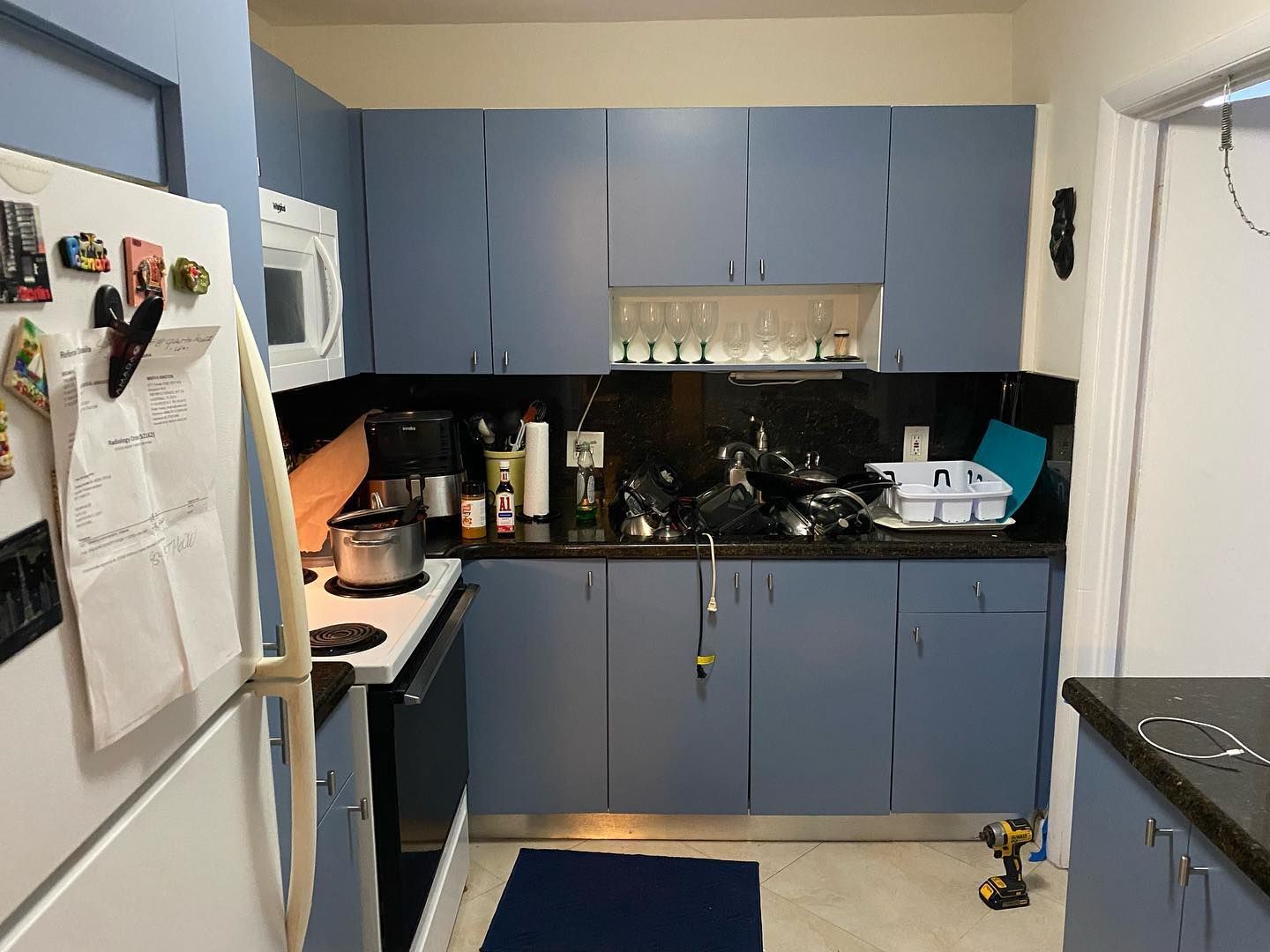 Blue kitchen cabinets with appliances, countertops, and a dark blue rug on the floor.