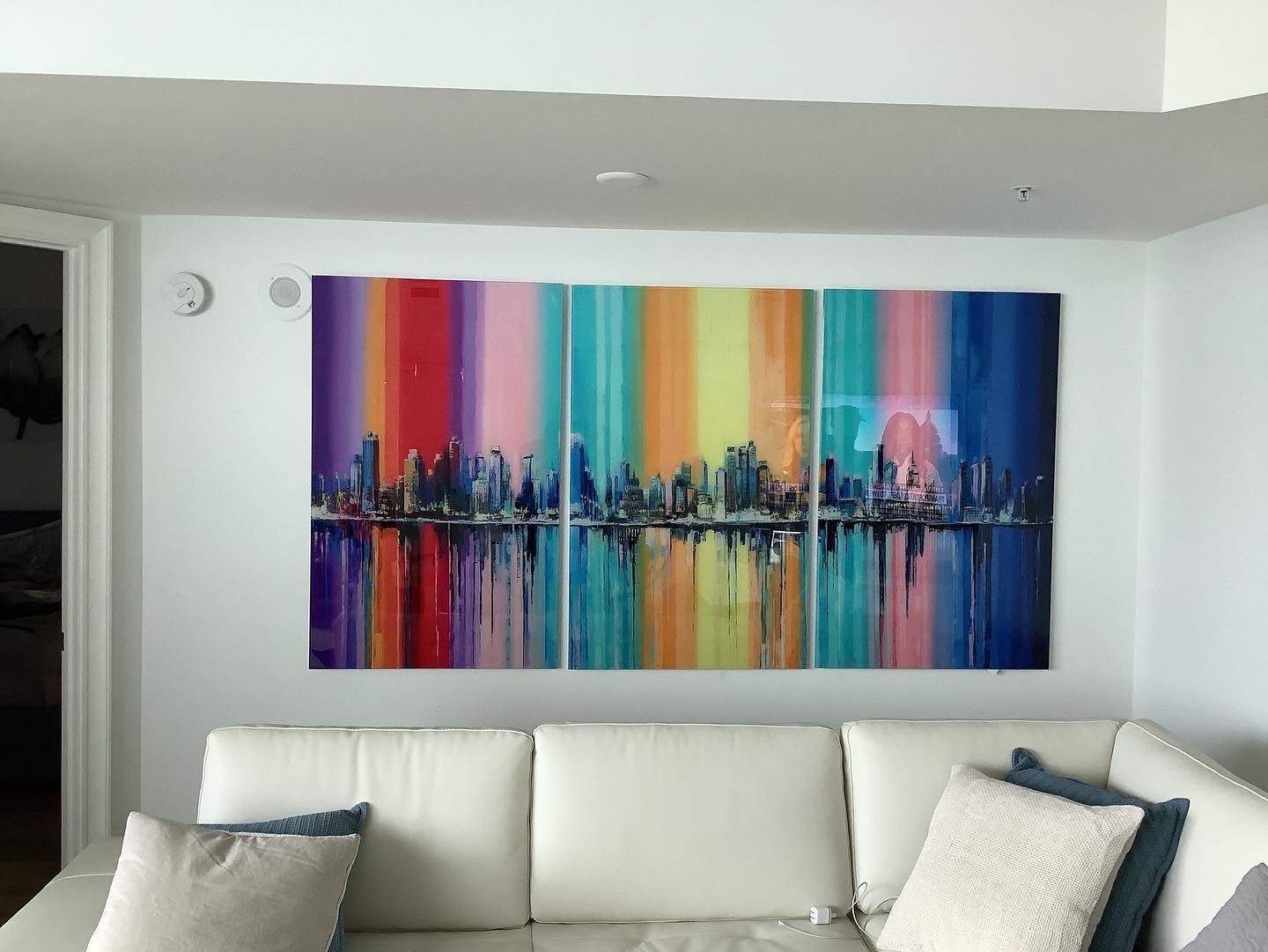 Colorful cityscape painting above white couch.