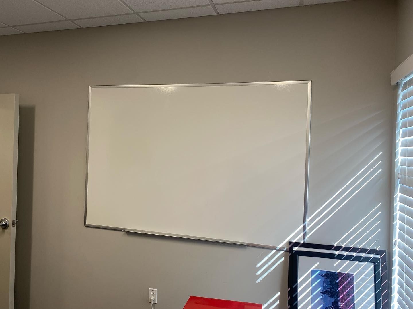 Whiteboard on a gray wall, with window and artwork below.