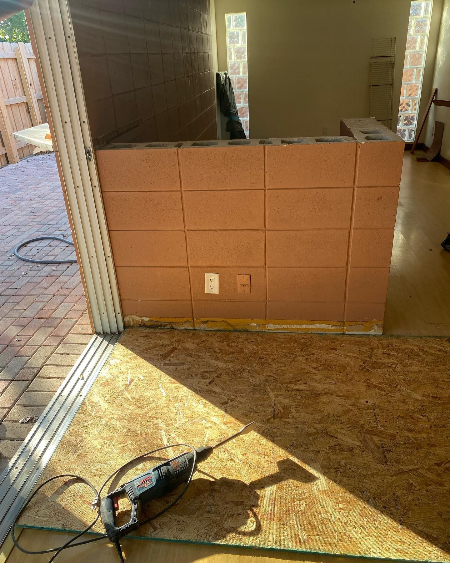 Construction site: brown brick wall with electrical outlets, power saw on OSB flooring.