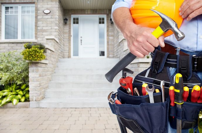 Handyman with tools and hard hat in front of a house.