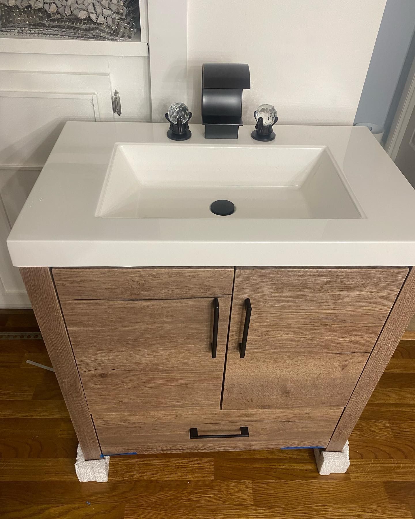 Wooden bathroom vanity with a white countertop and black fixtures.