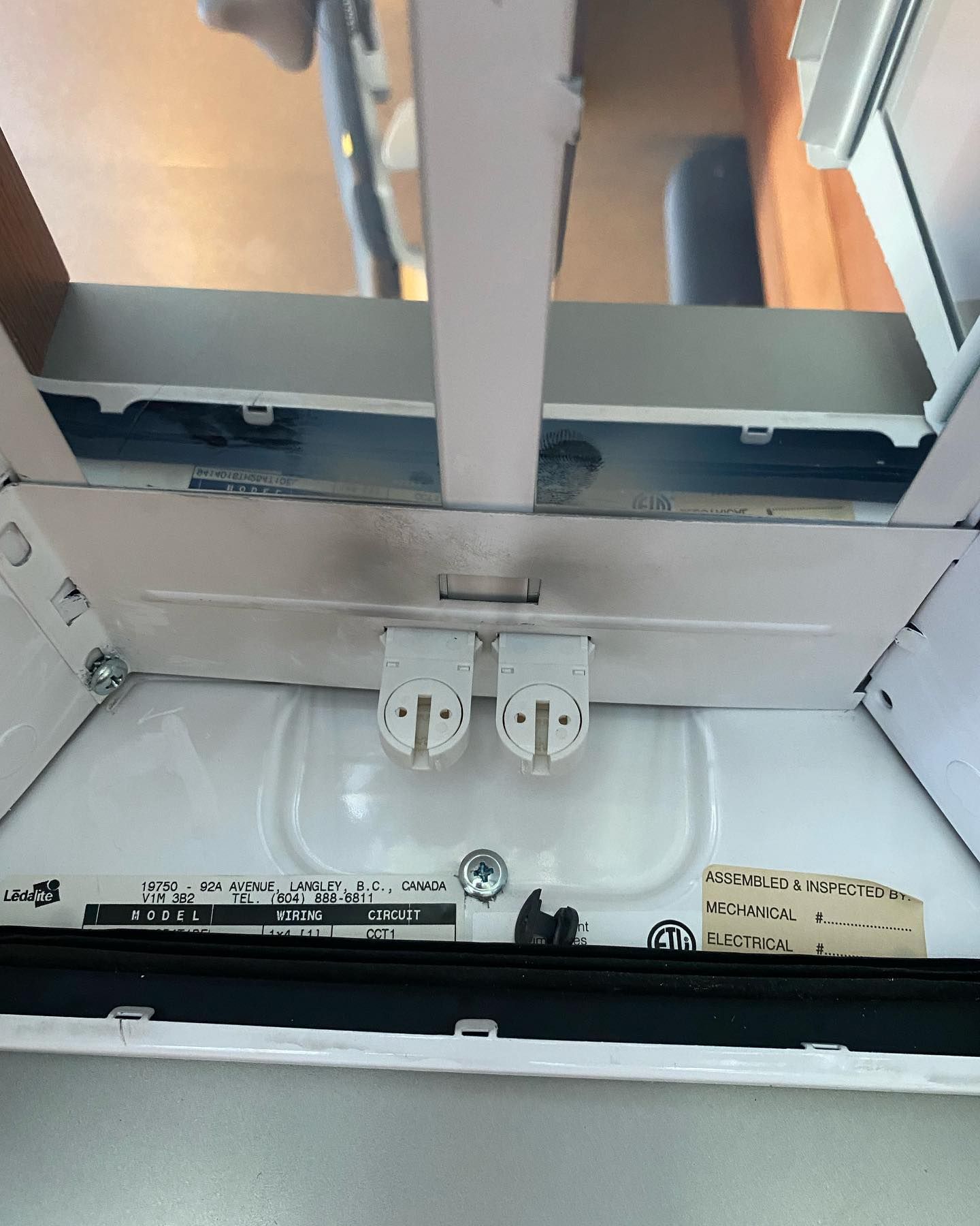 Overhead view of a fluorescent light fixture; white with two bulb sockets.