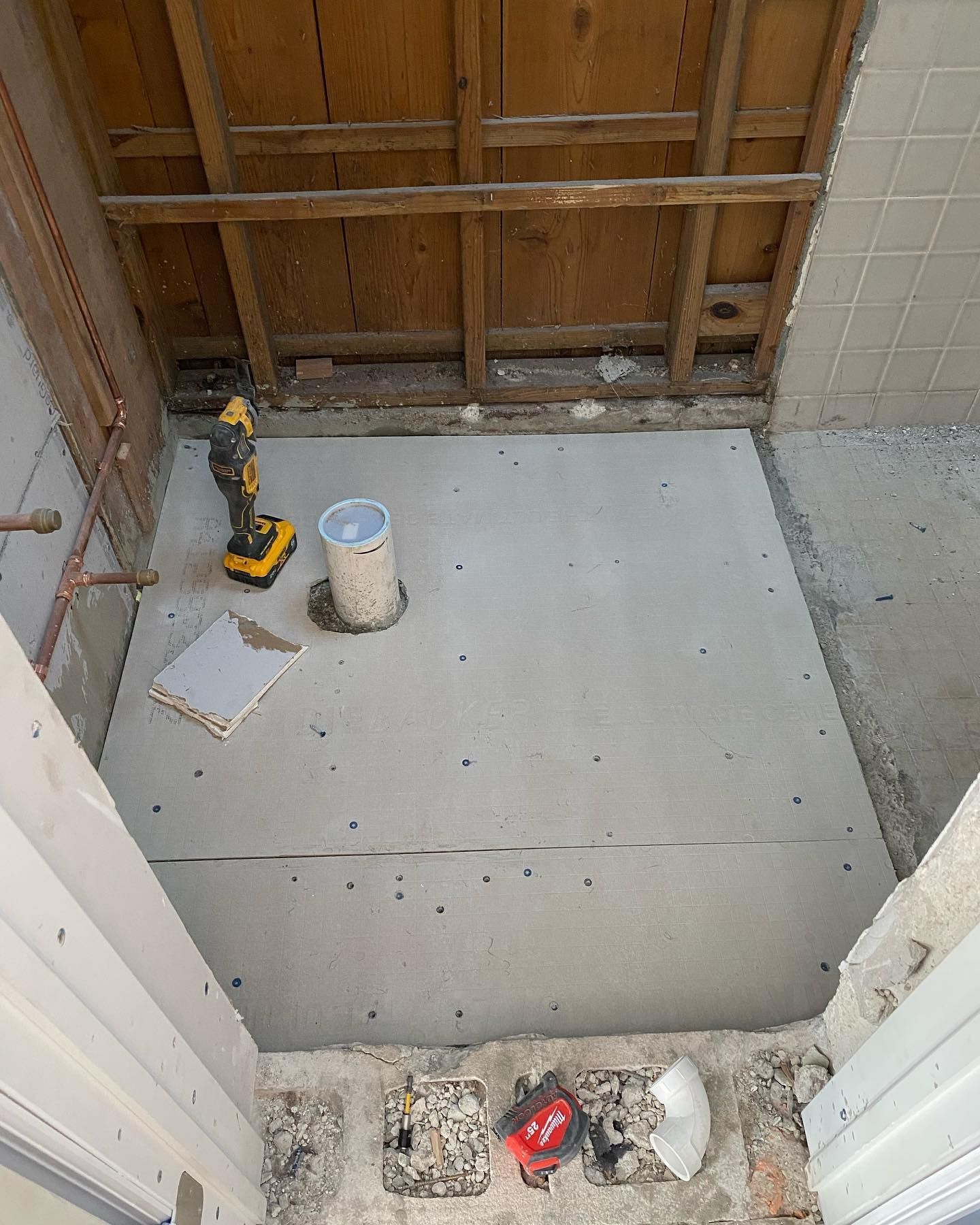 Bathroom under construction with concrete floor, exposed wood framing, and tools scattered about.