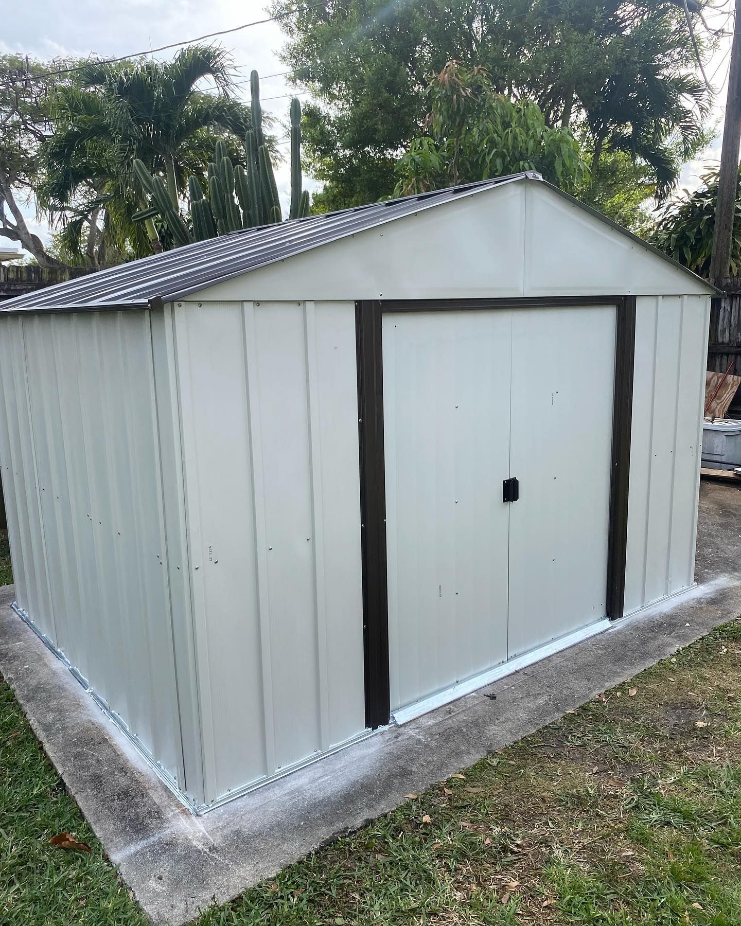 Tan metal storage shed with brown door frame and black handle on a concrete pad.