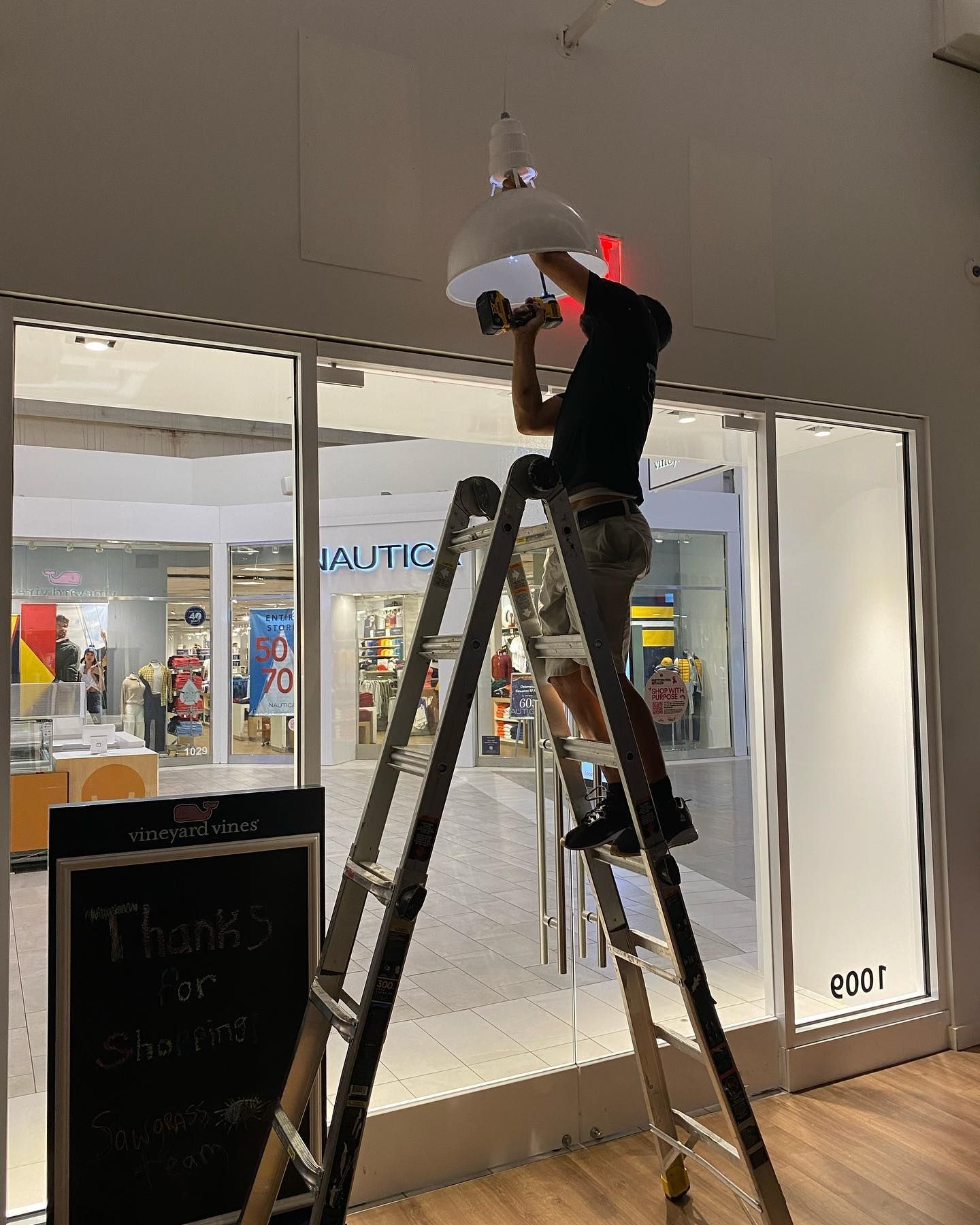 Person on a ladder installing a light fixture inside a store entrance.