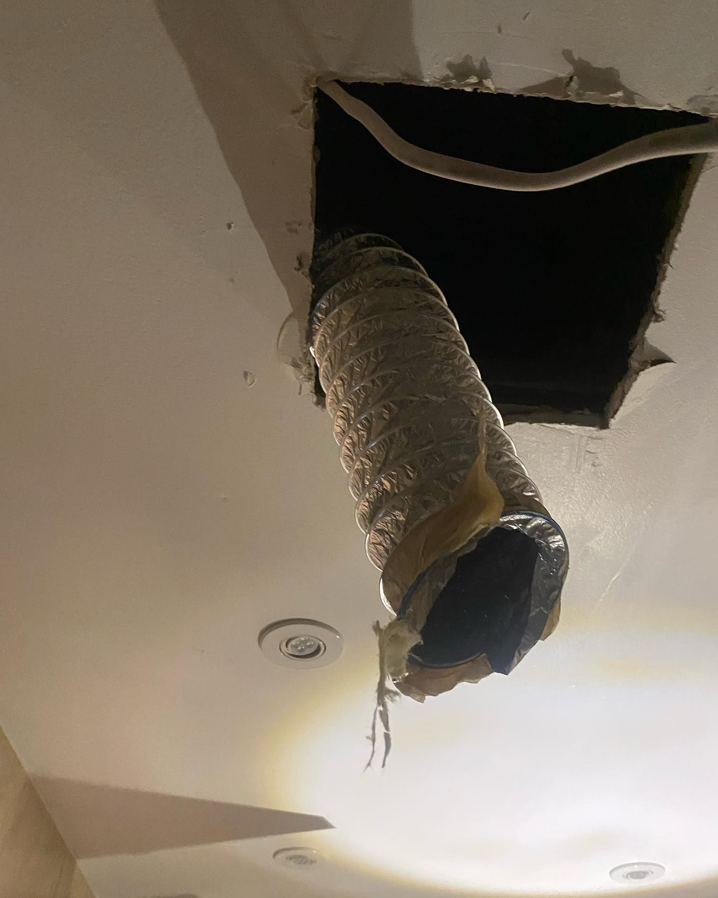 Ceiling with a damaged square hole exposing a silver, flexible duct. Electrical wires visible.