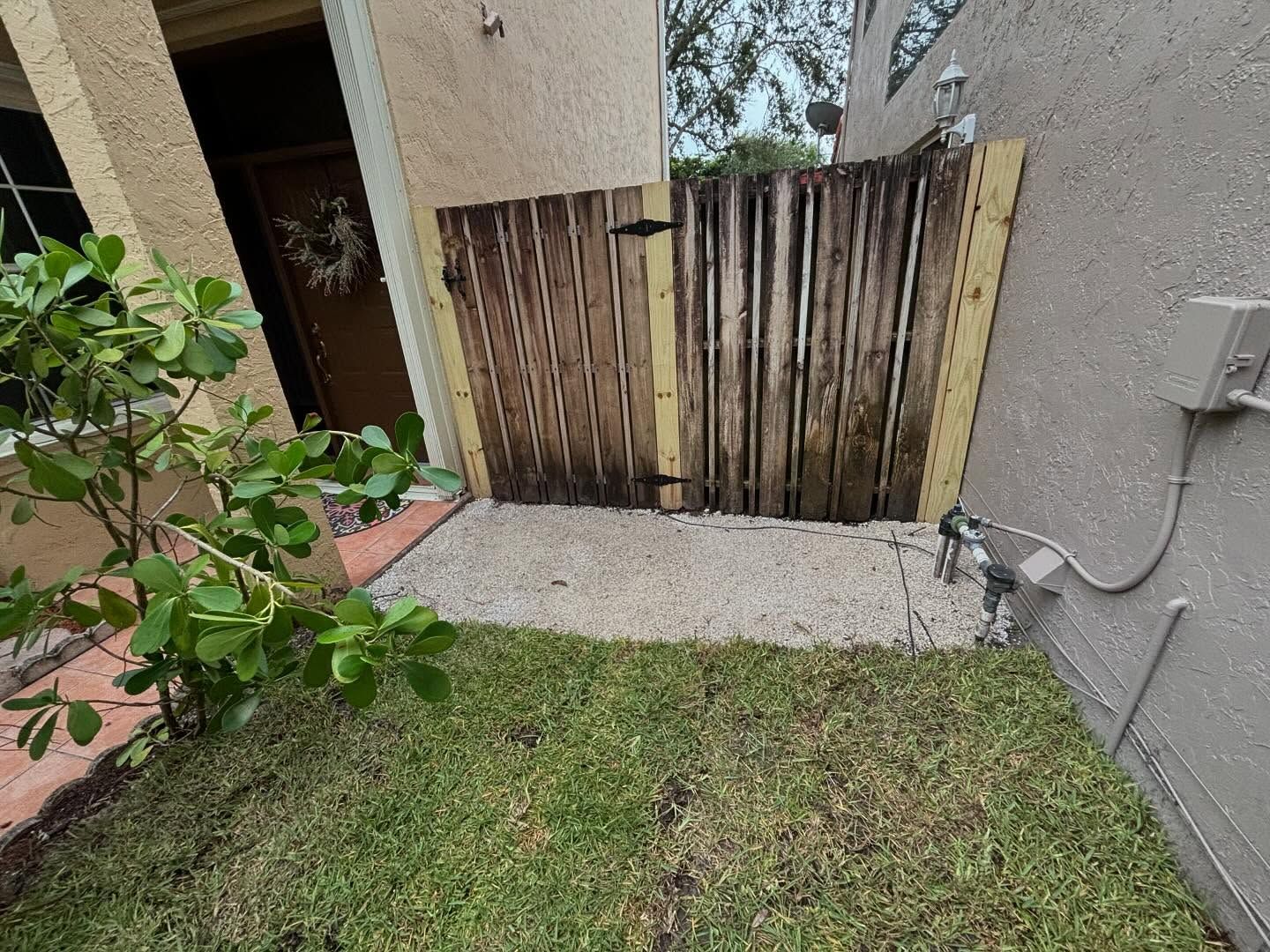 Wooden gate in a small yard, opening to gravel. Green grass and stucco building surround it.