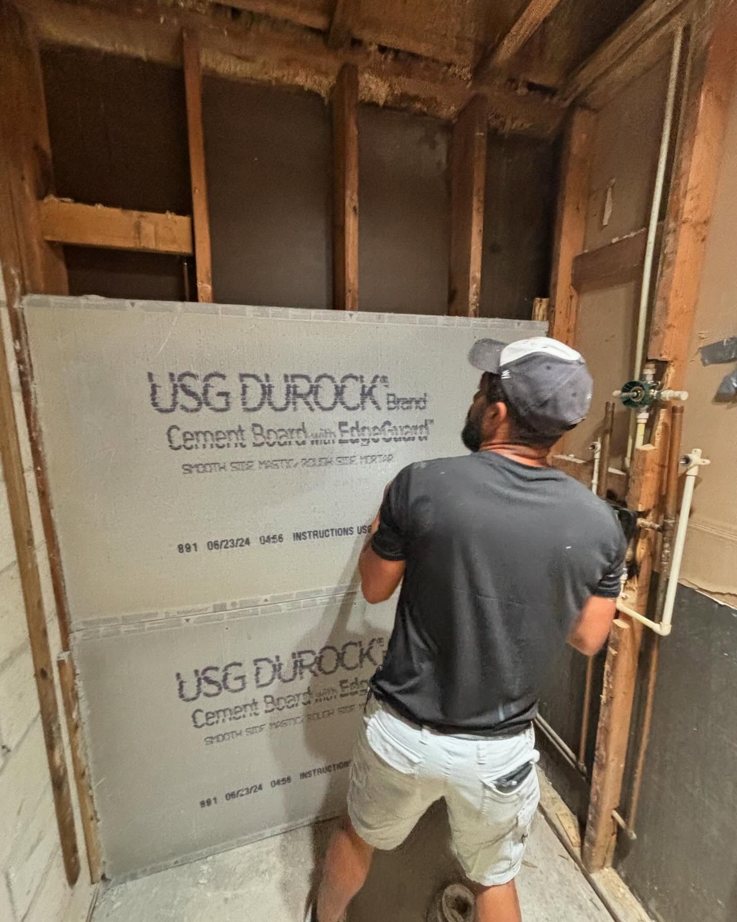 Man installing USG Durock cement board in a bathroom with exposed studs.