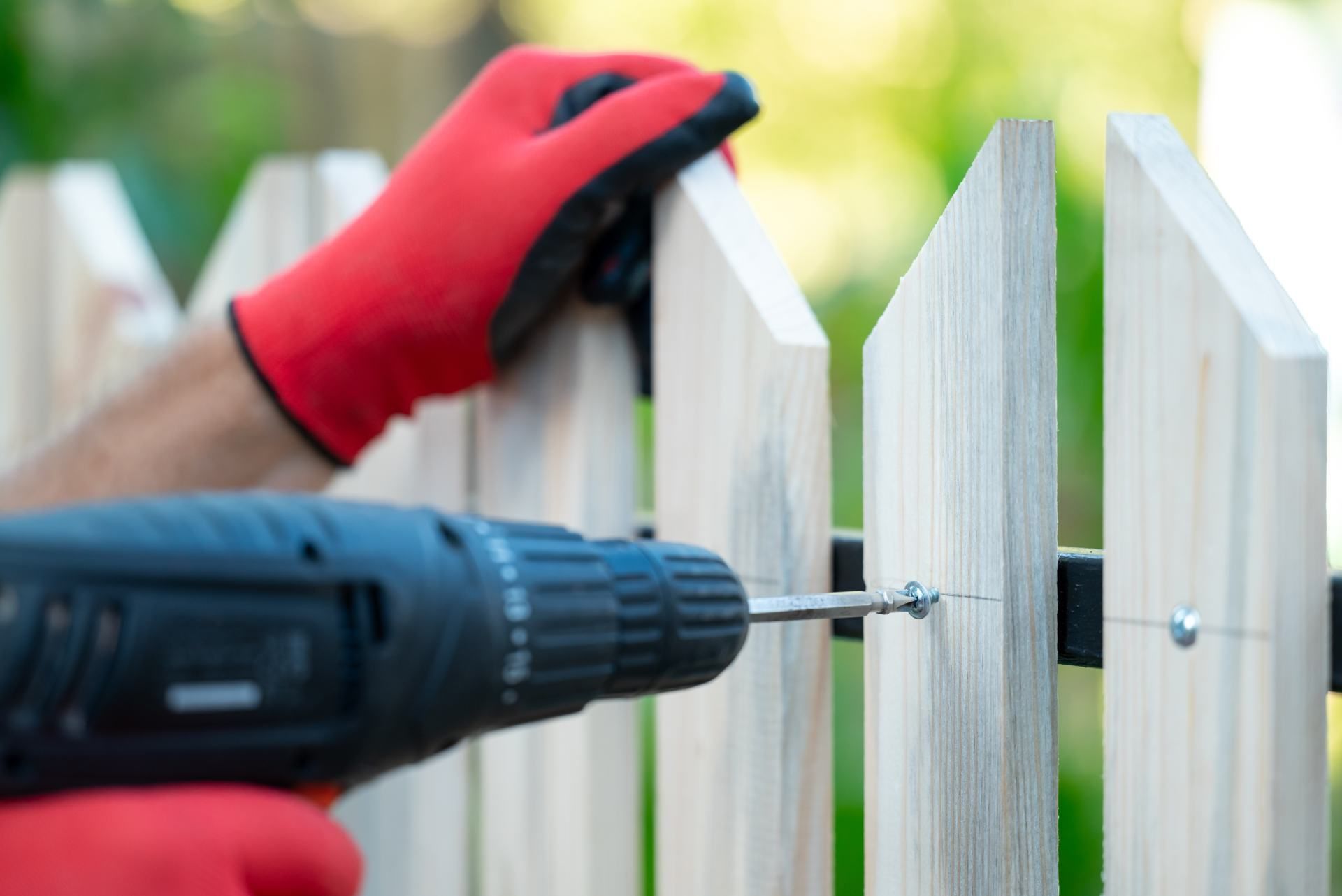 Person in red gloves using a drill to attach a picket fence.