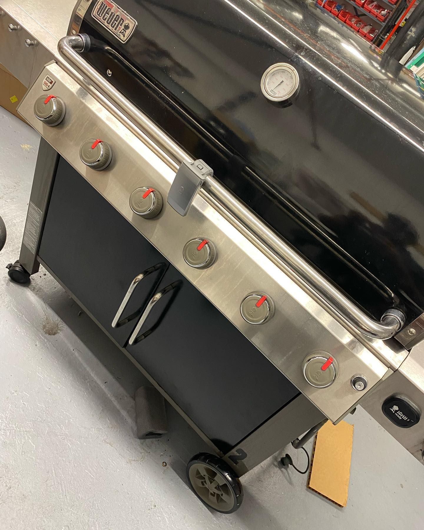 Black grill with six burner knobs, stainless steel accents, and a thermometer.