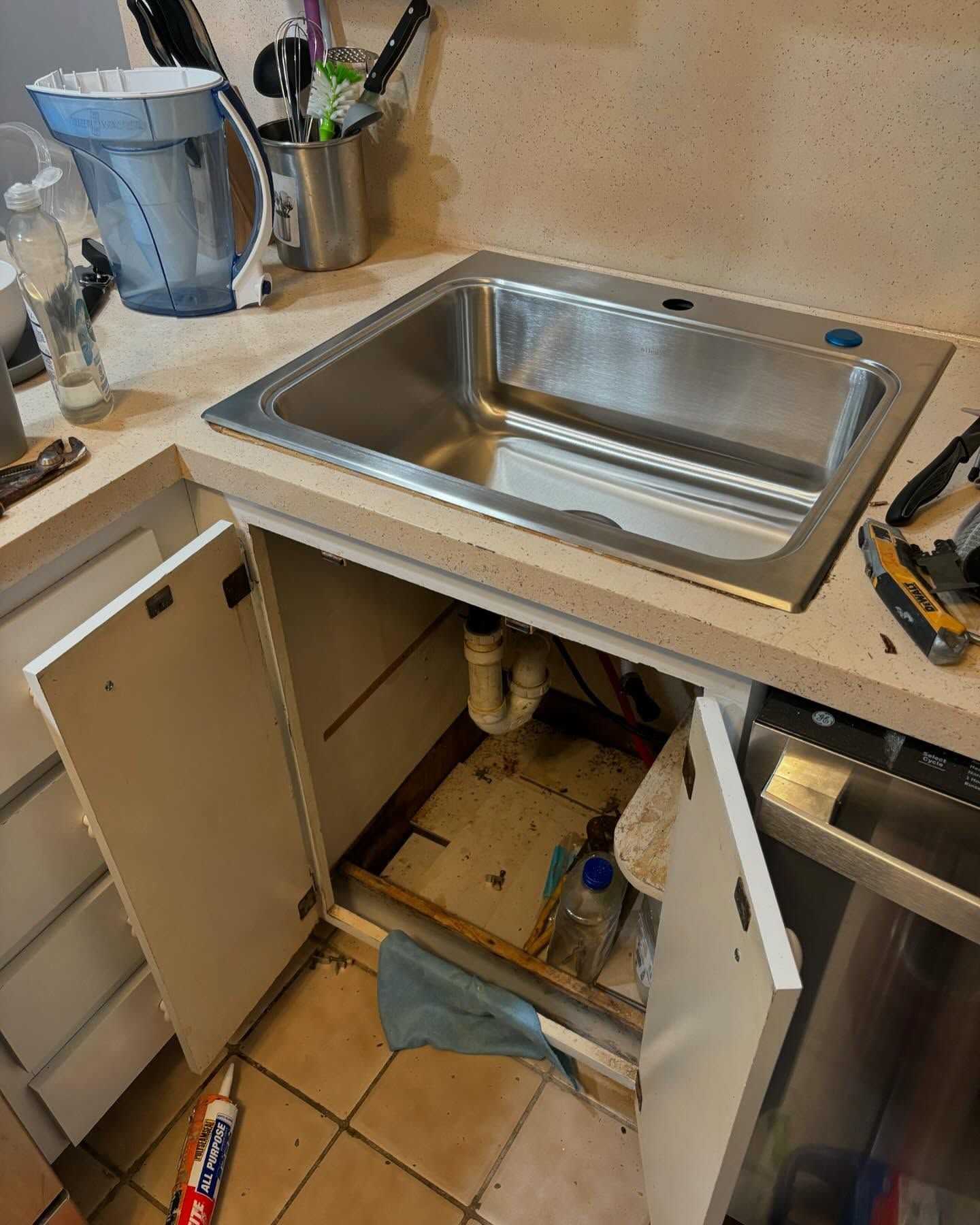 Kitchen sink with open cabinet doors. Plumbing and cleaning supplies visible.
