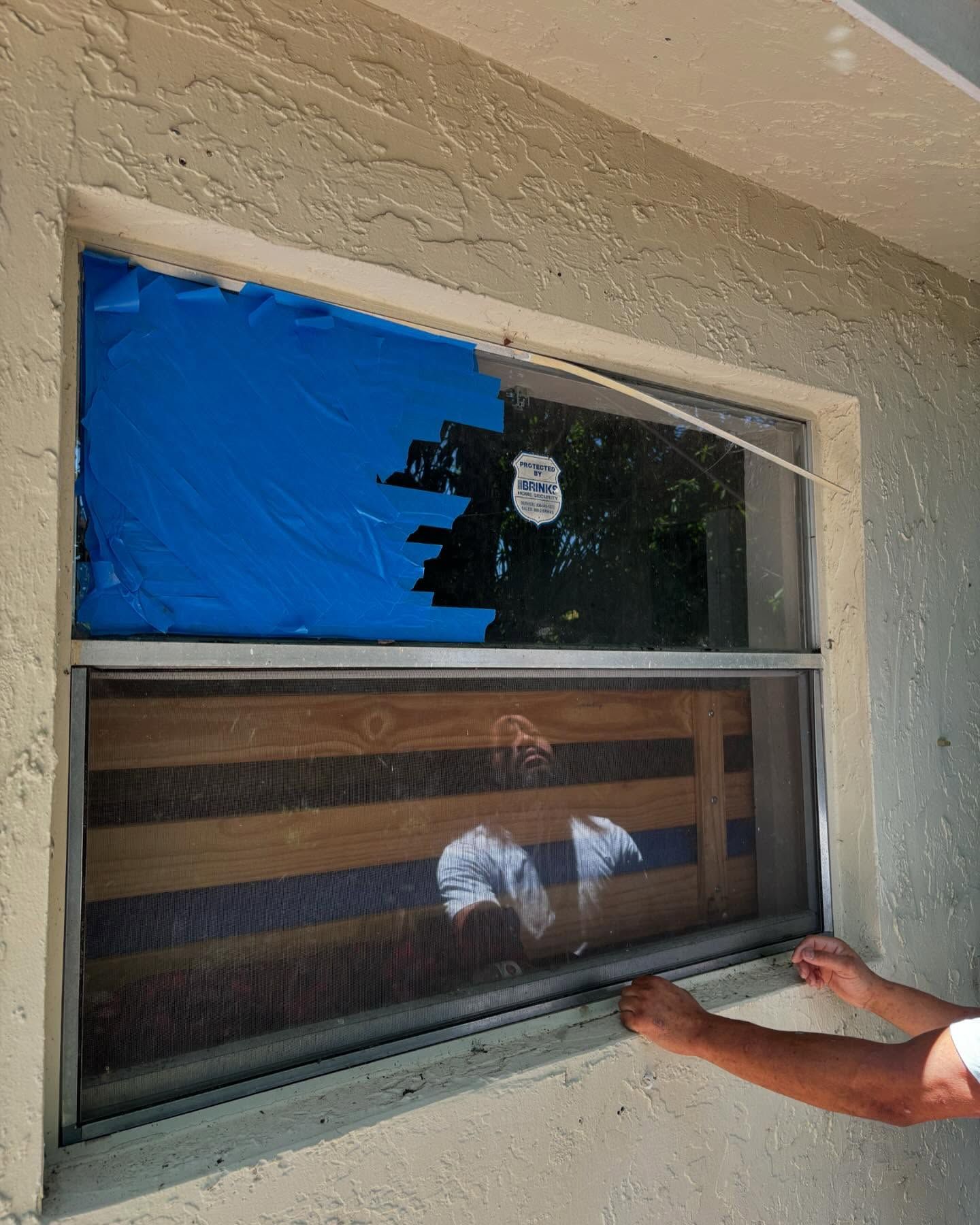 Window damage: Blue tarp covers broken glass, lower section boarded up, person adjusts screen.