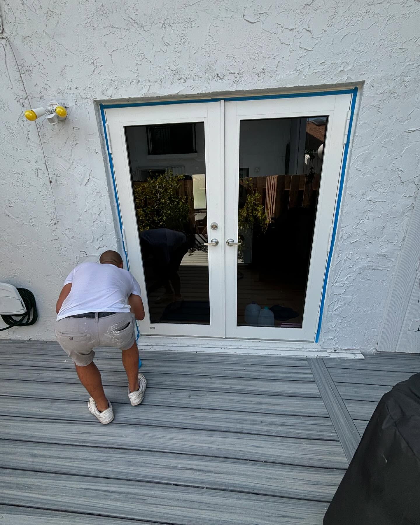 Man installing or inspecting white French doors on a deck. The opening is angled.