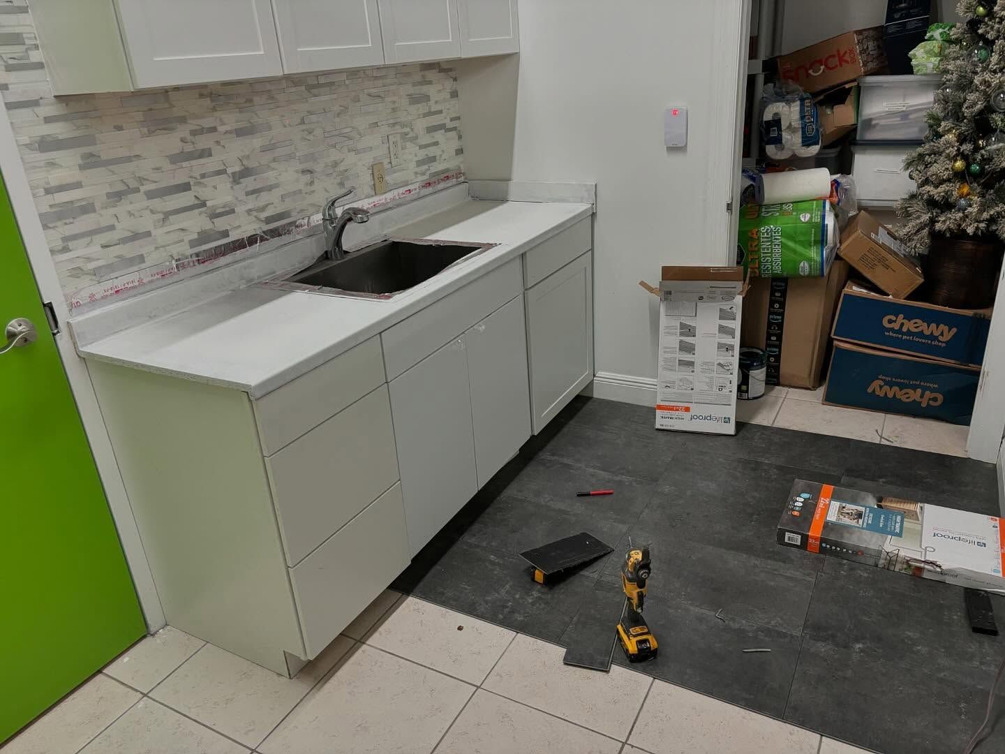 White kitchen cabinets with a sink, tools, and a green door.