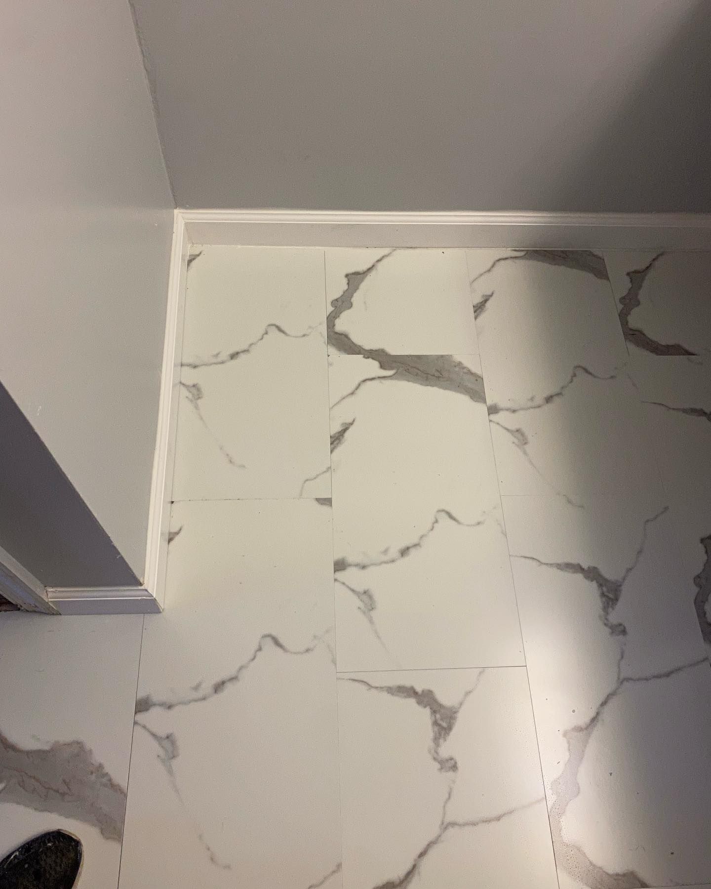 White marble tile floor with gray veining, beside a white wall with trim.