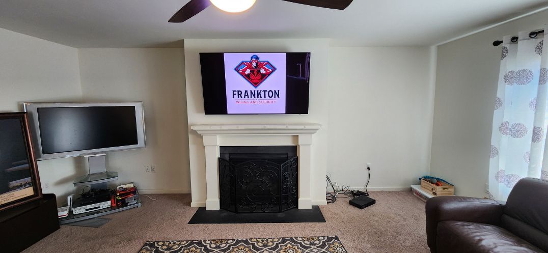 Living room with fireplace, TV, brown sofa, and wall-mounted screen above mantel