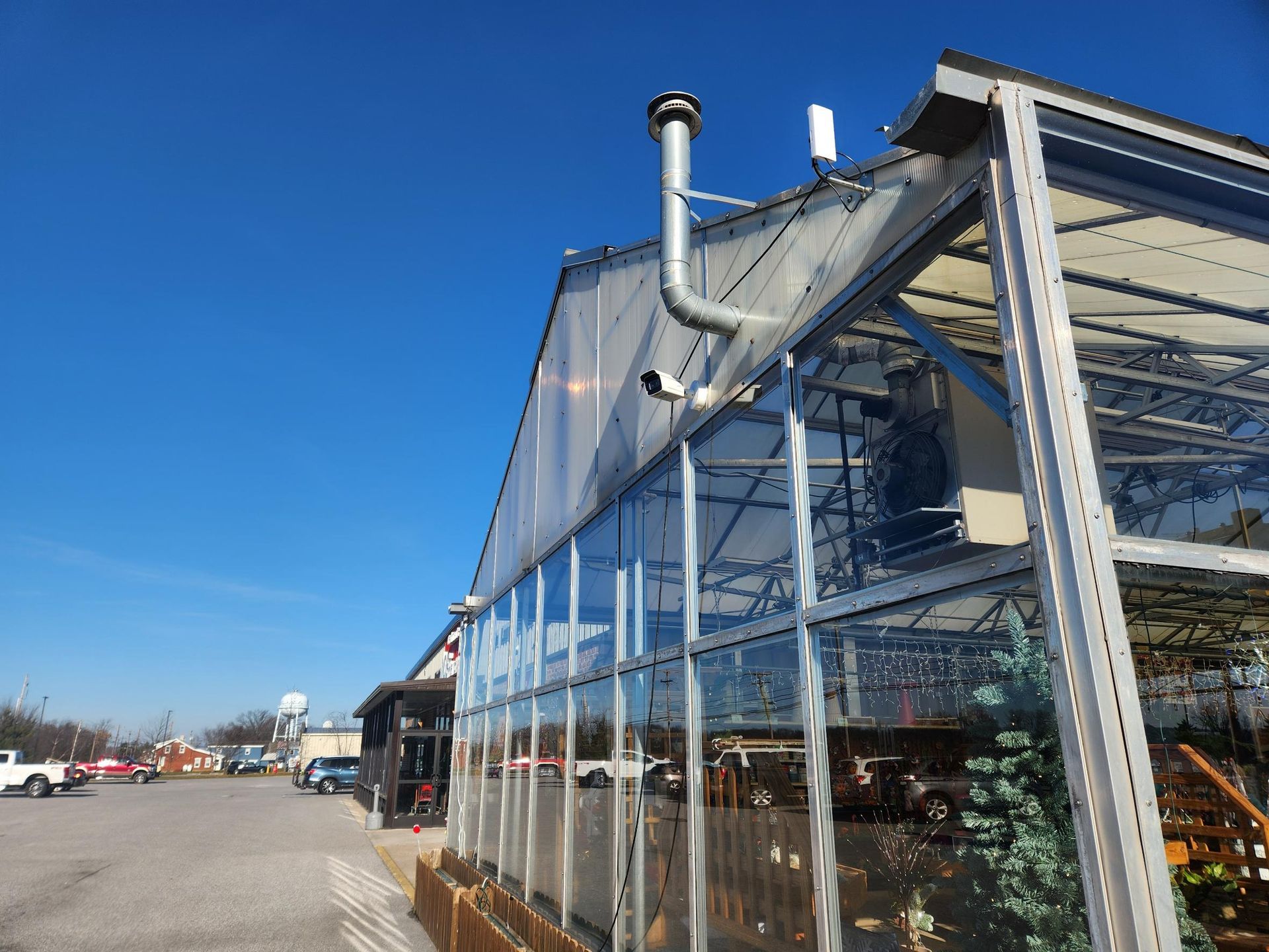 Glass greenhouse storefront beside a parking lot under a clear blue sky