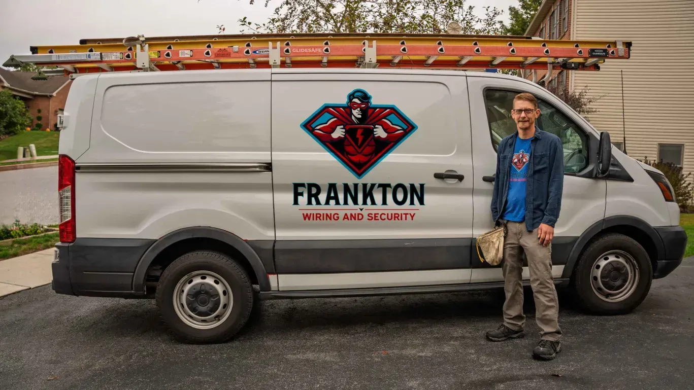 Man standing beside a white work van with ladder racks and FRANKTON logo in a parking lot