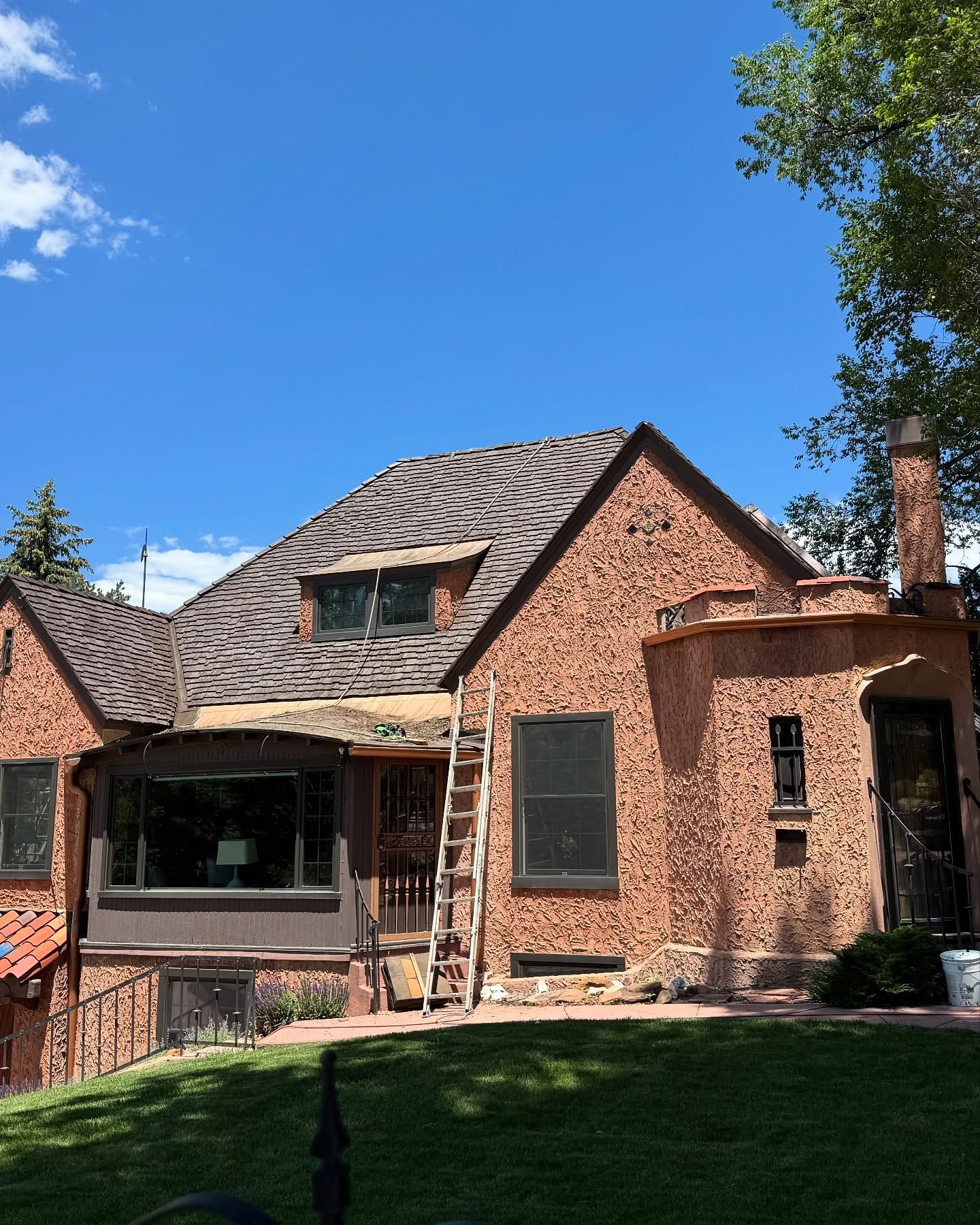 Brick house with shingled roof, front porch, and ladder, set in a sunny yard under a clear blue sky