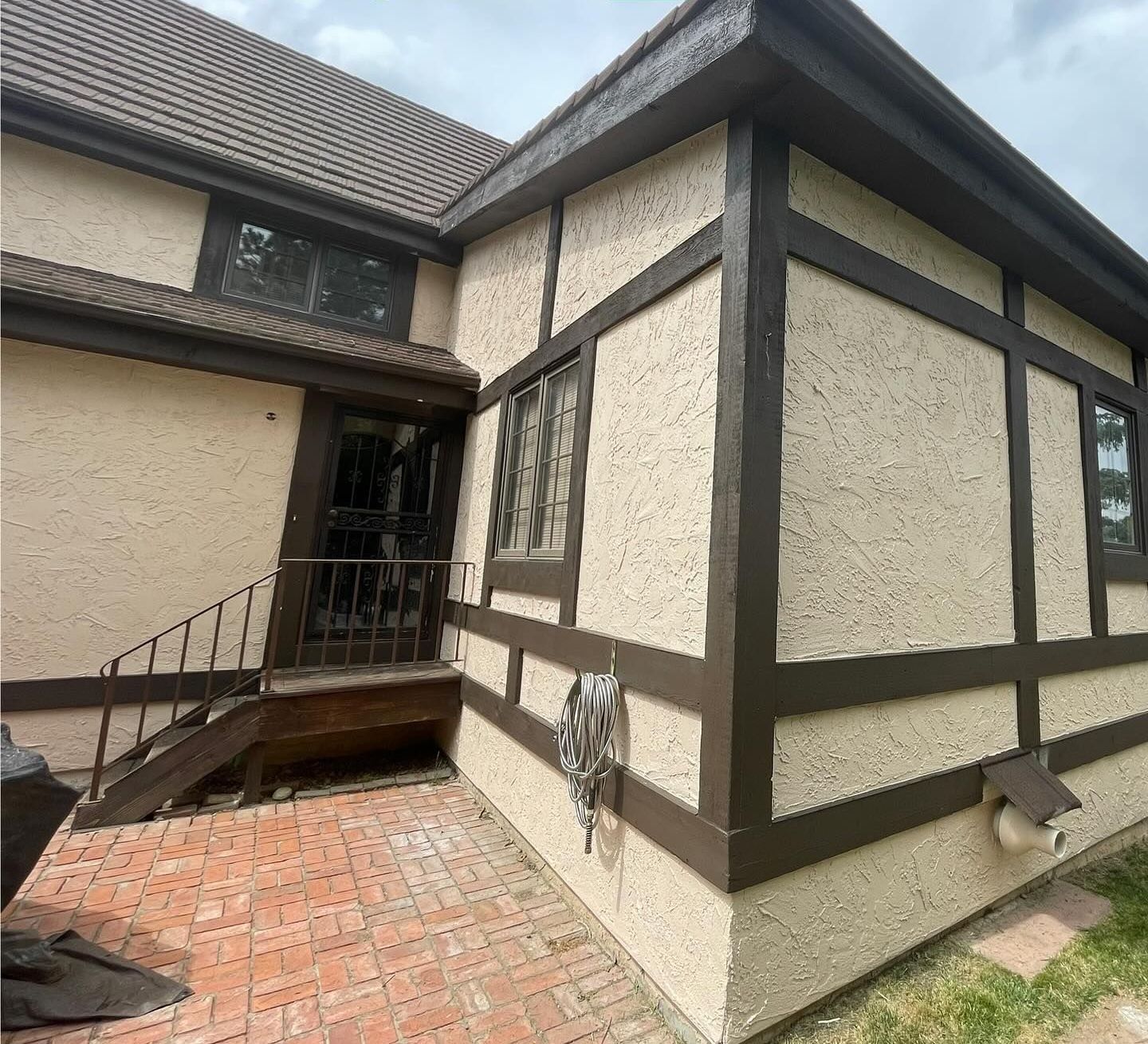Exterior corner of a house with cream stucco and dark trim, a small porch, and a brick patio.