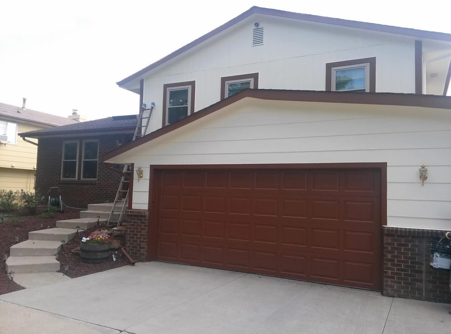 Two-story house with white siding, brown garage door, and front steps leading to the entrance