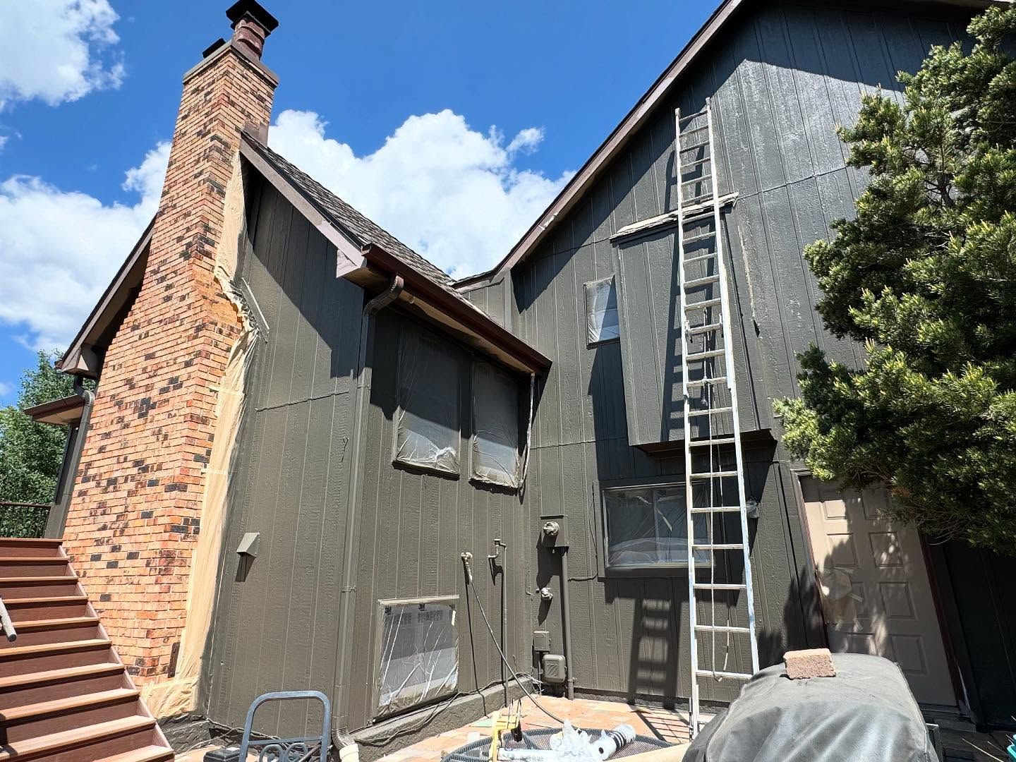 Exterior of a house with a brick chimney, gray siding, and a ladder leaning against the upper wall