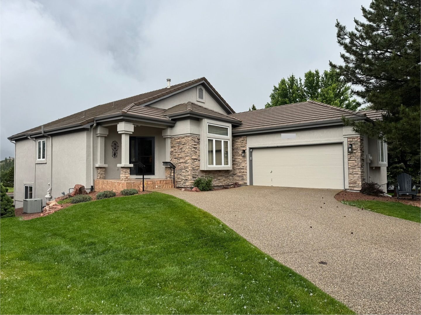 Single-story suburban house with beige exterior, white garage, green lawn, and overcast sky