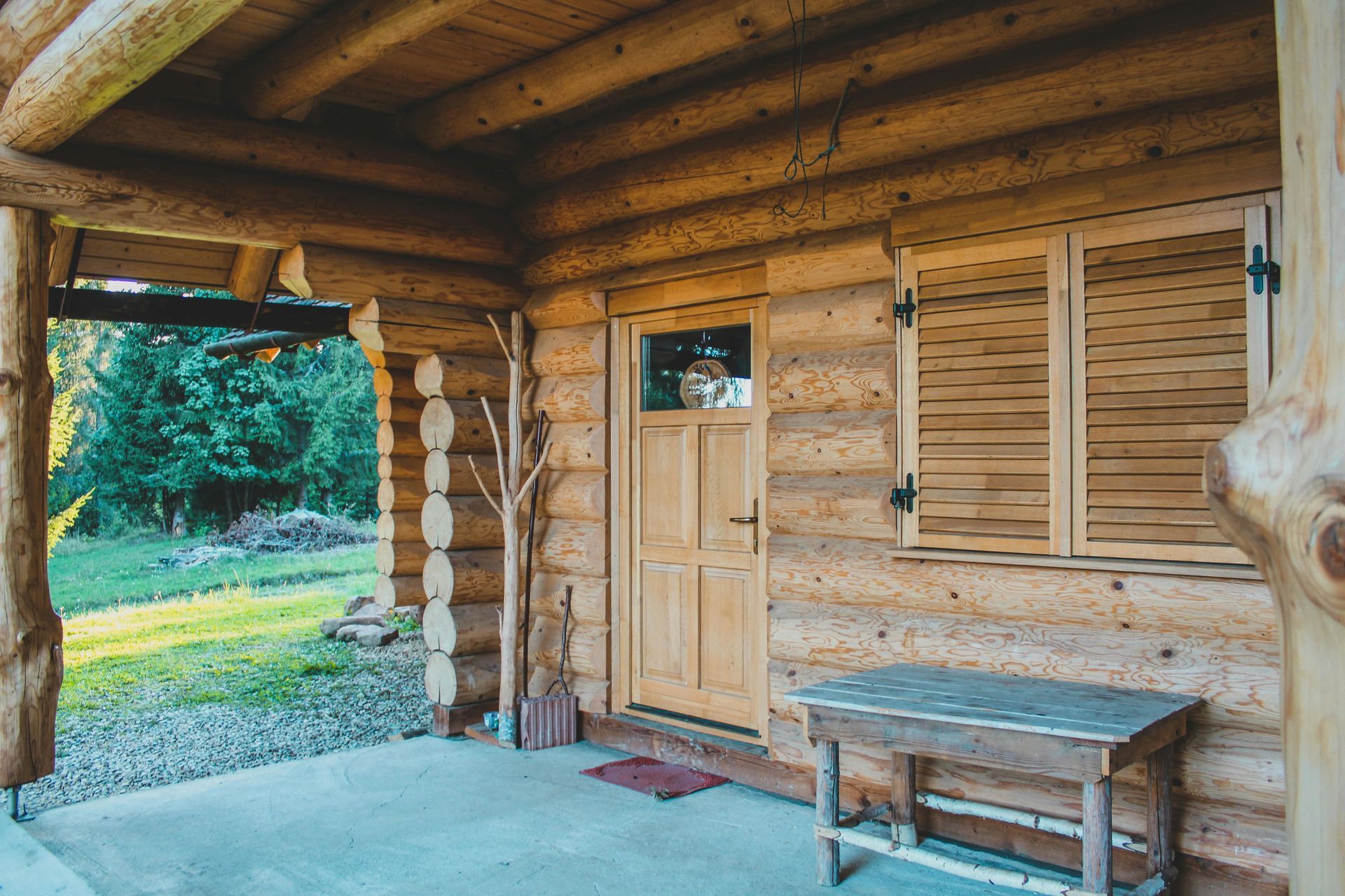 Wooden porch with log walls, a bench, and a closed door, overlooking a grassy yard.