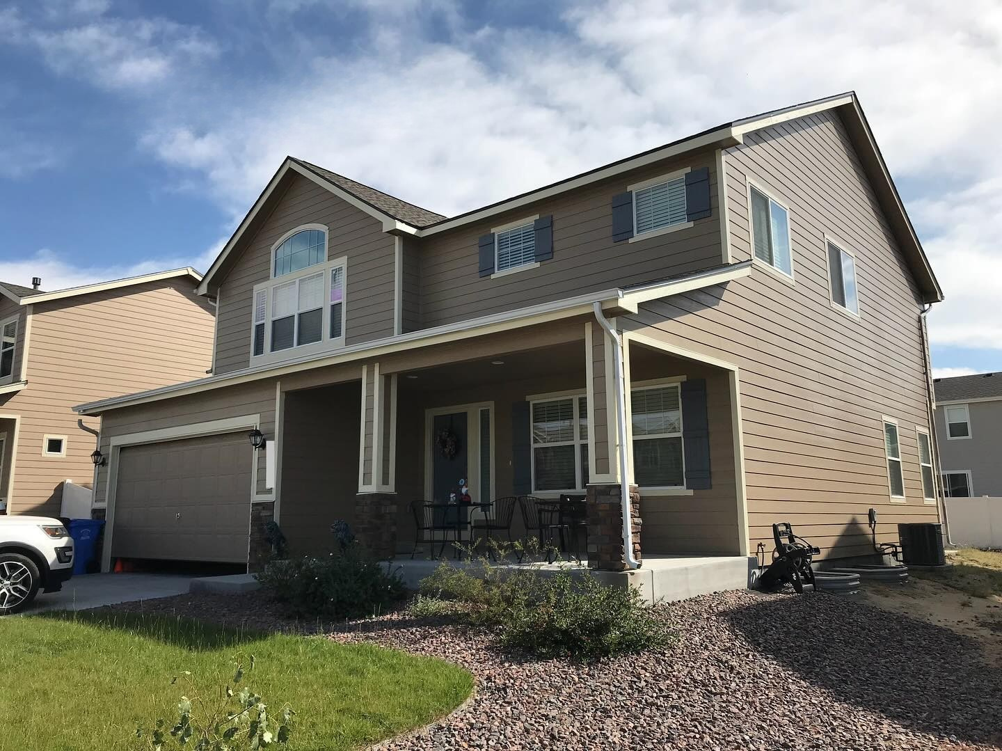 Two-story beige house with a covered front porch, attached garage, and landscaped front yard.