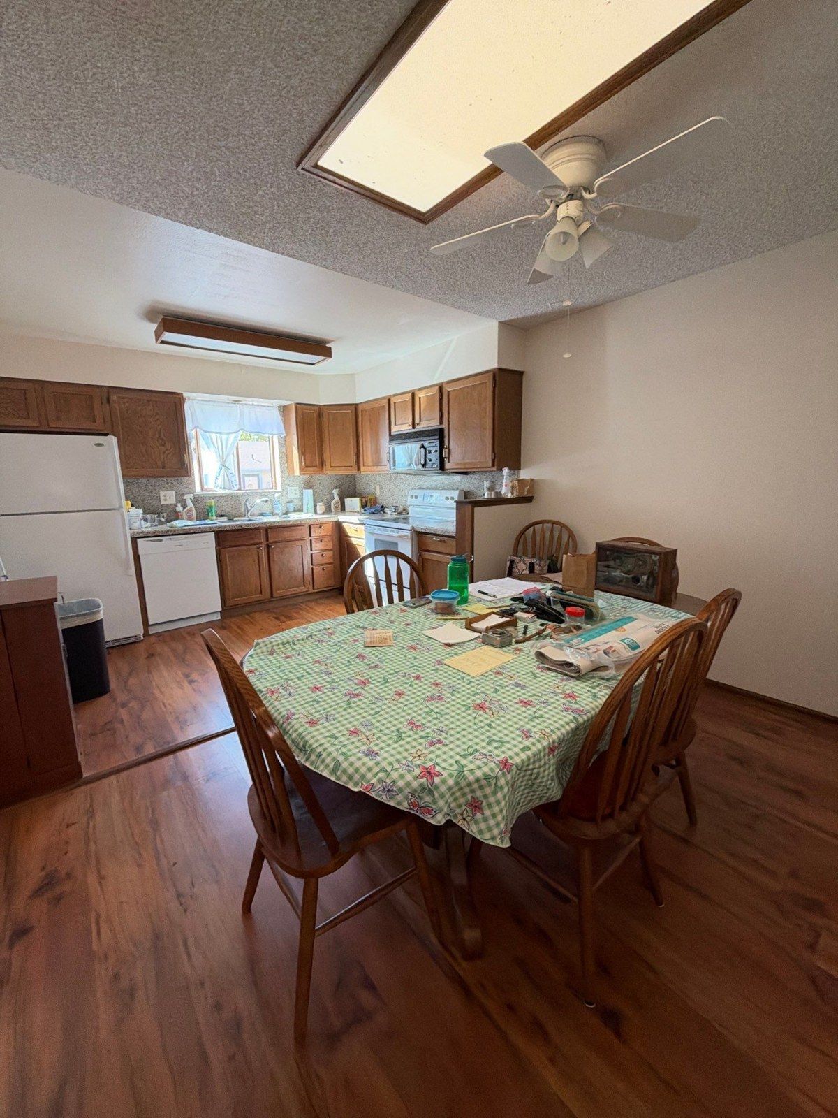 Kitchen and dining area with wood cabinets, table, flooring and ceiling fan before the proposed interior painting