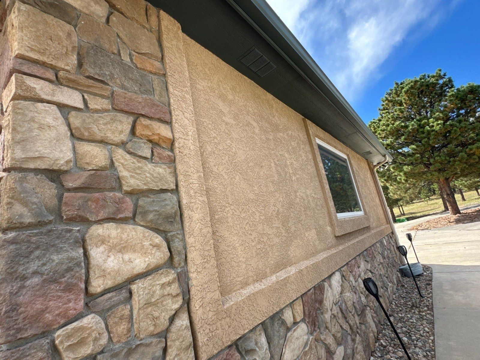 Existing stone beside stucco, a window and roof-edge trim in a Larkspur exterior painting proposal