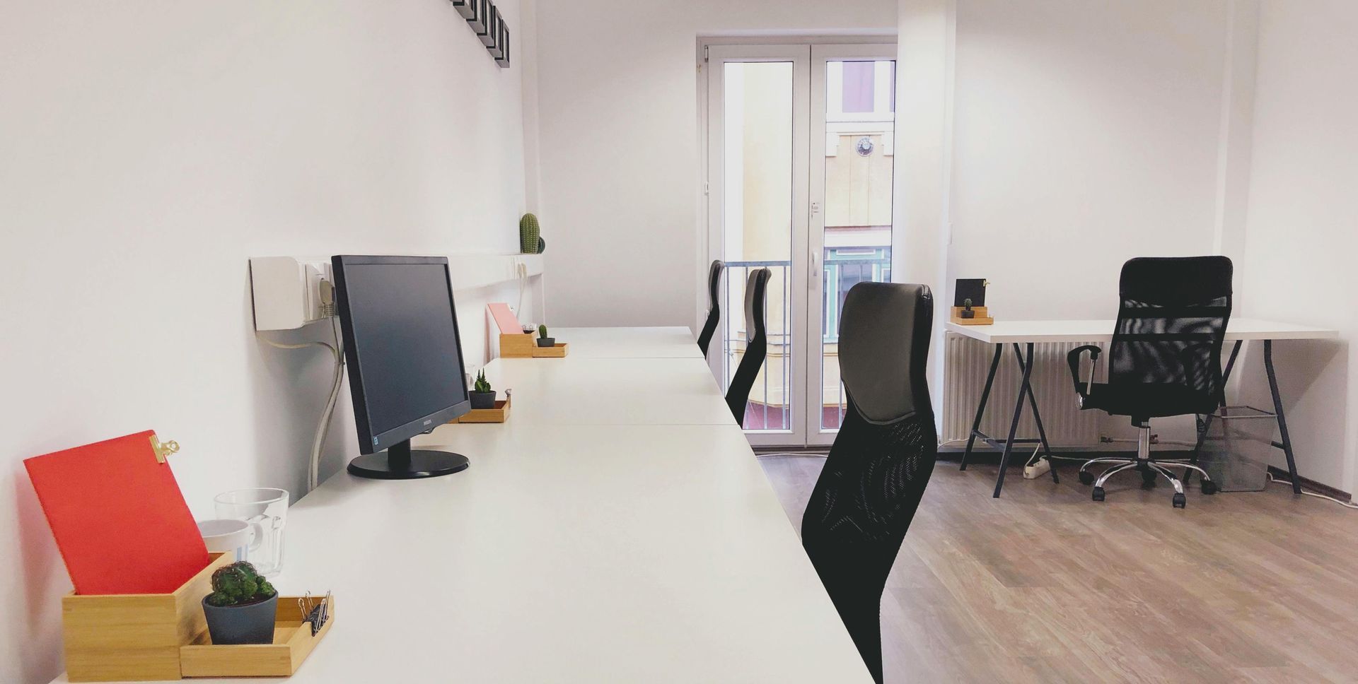 Bright minimalist office with white desks, black chairs, and a computer near a doorway