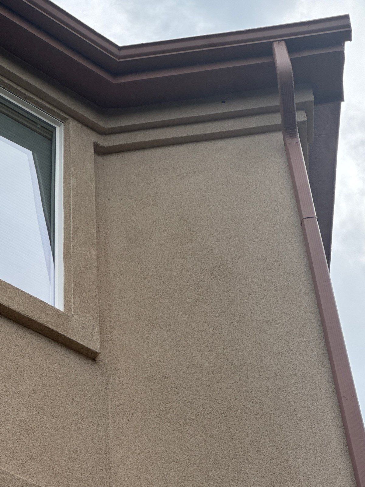 Existing stucco corner beside downspout and roof-edge trim in the same exterior estimate
