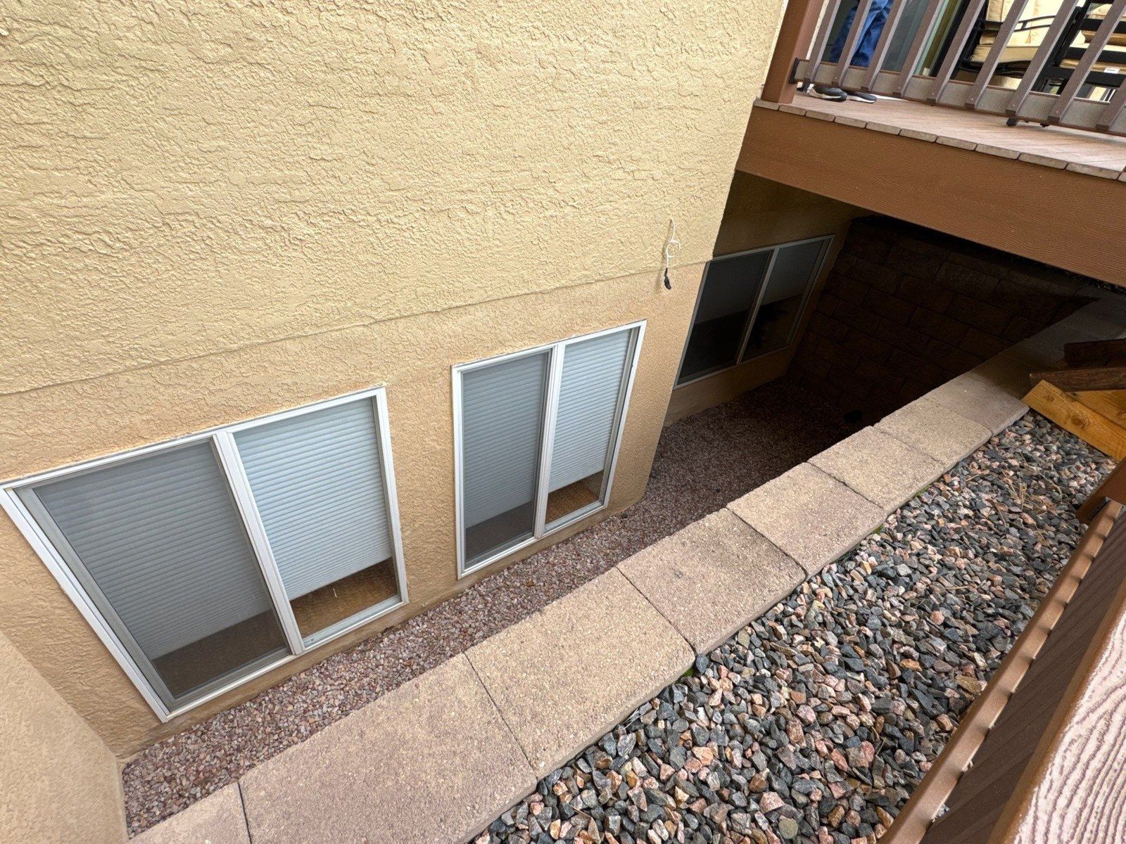 Lower stucco wall and basement windows beside gravel and the deck at the same property